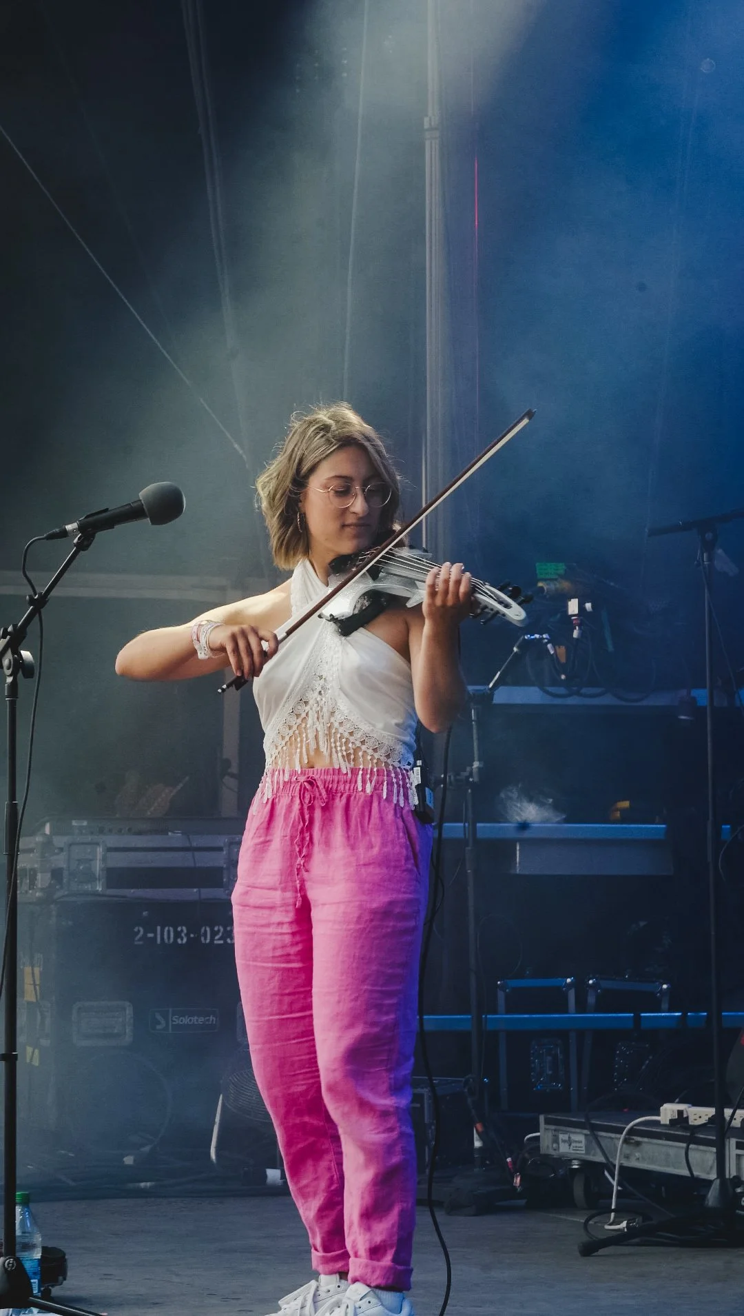 Marianne Paquin joue du violon sur scène à Osheaga dans un concert, portant un haut blanc à dentelle et un pantalon rose.