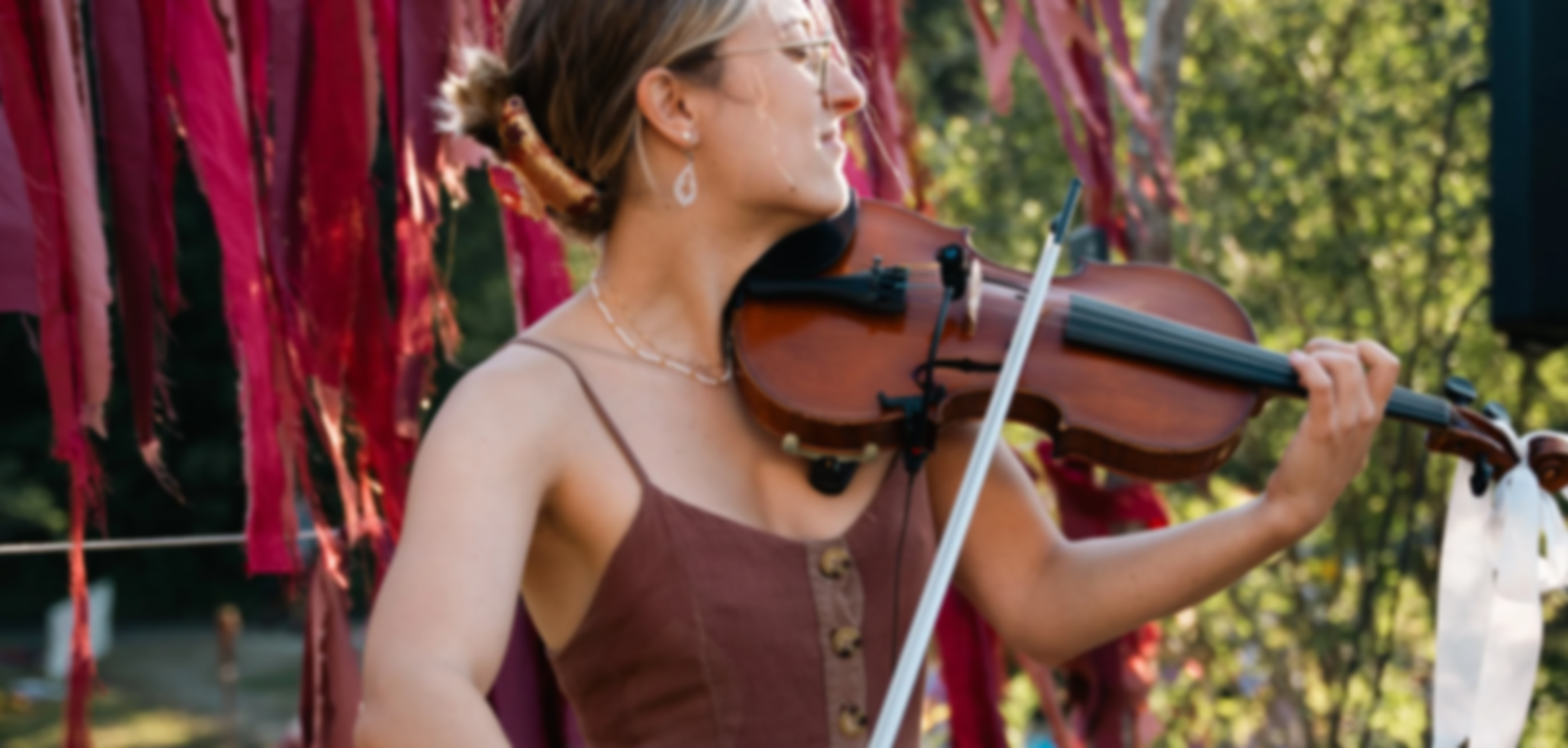 Une femme jouant du violon dans un environnement extérieur, avec des tissus de couleurs vives suspendus derrière elle.