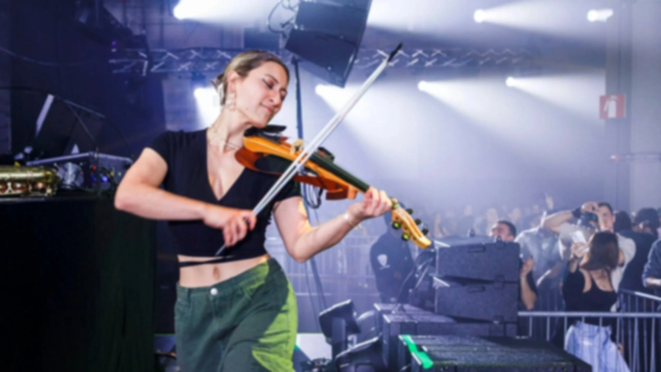 Marianne Paquin joue du violon électrique lors d'un concert dans une salle bondée, avec des lumières de scène et des spectateurs en arrière-plan.