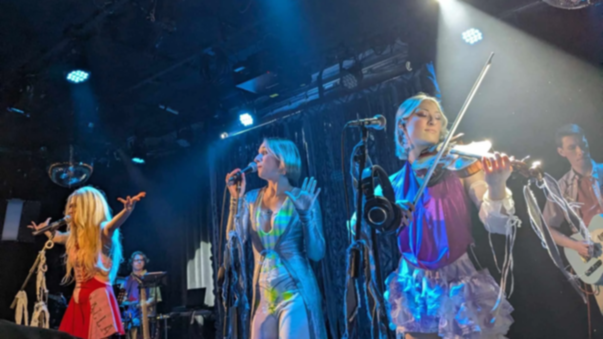 Groupe de musiciens sur scène lors du lancement d'album d'Éléonore Lagacé. Trio de jeunes femmes à l'avant, deux chanteuses et une violoniste.