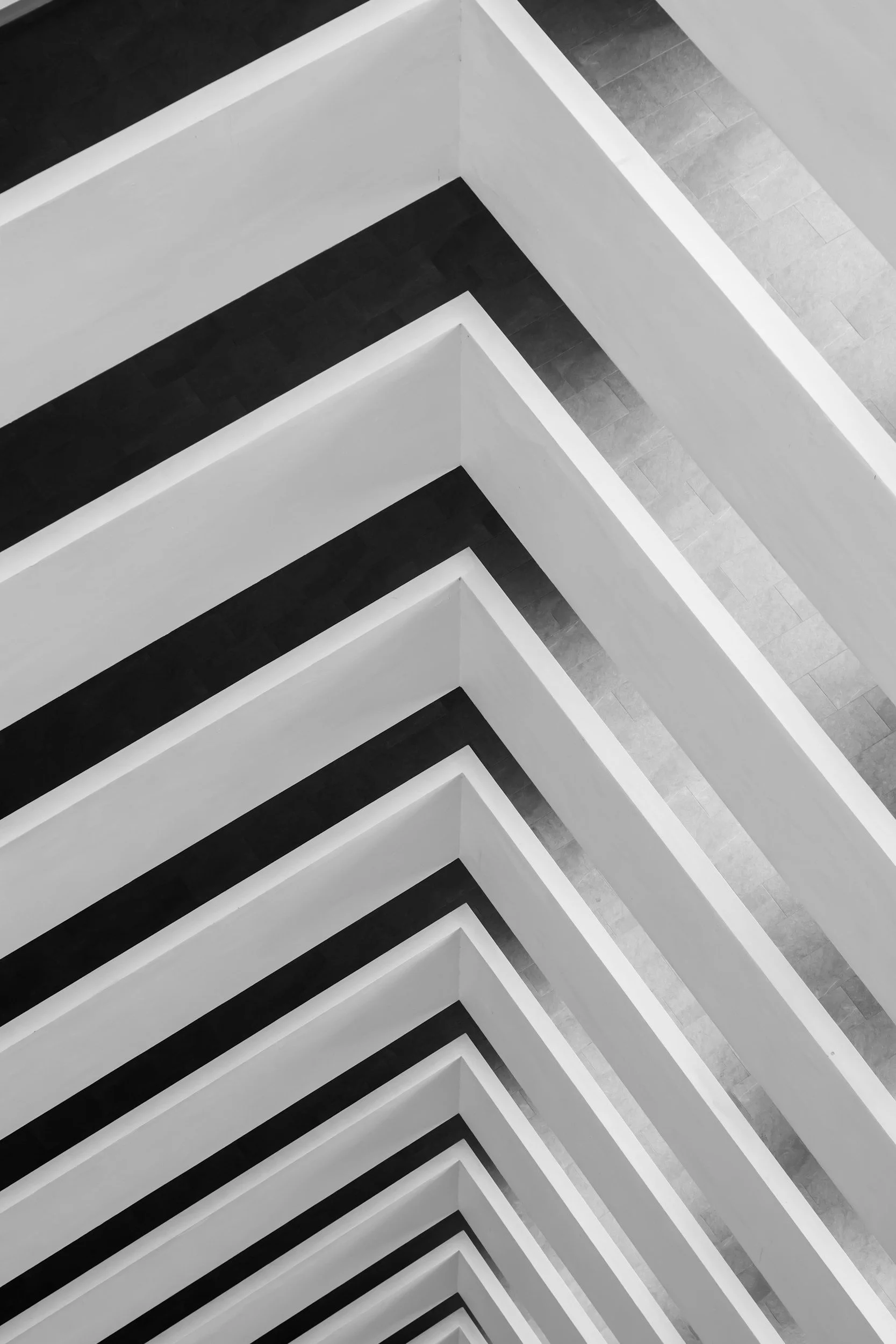 Black and white photograph of geometric architectural structure with repeating patterns of white and black rectangular beams or supports, creating a series of parallel lines and sharp angles.