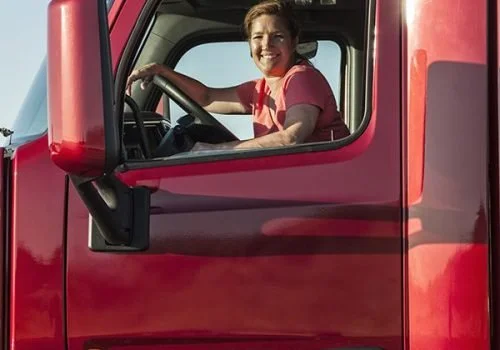 A woman smiling and waving while sitting in the driver's seat of a red truck.