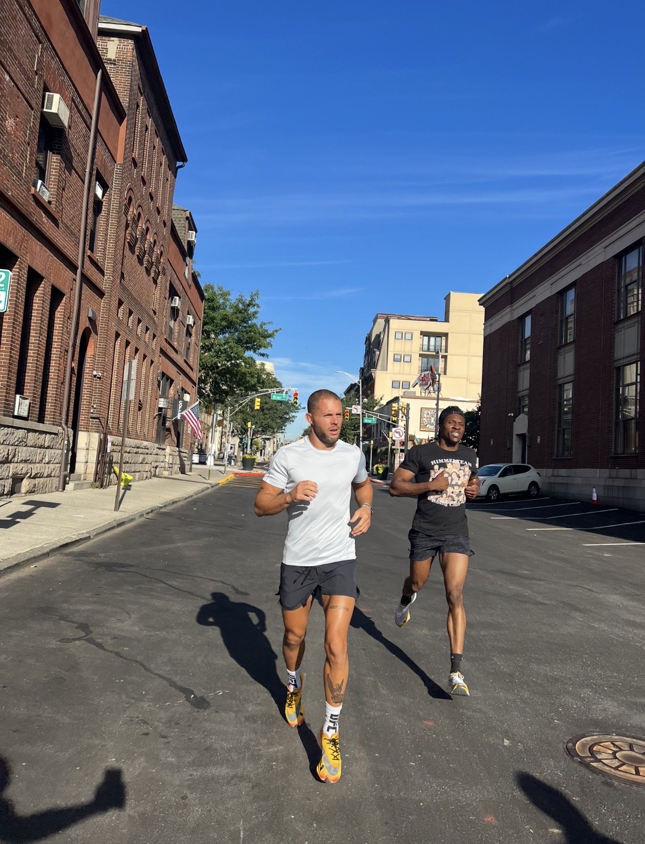 Two men jogging down a city street between brick buildings on a sunny day