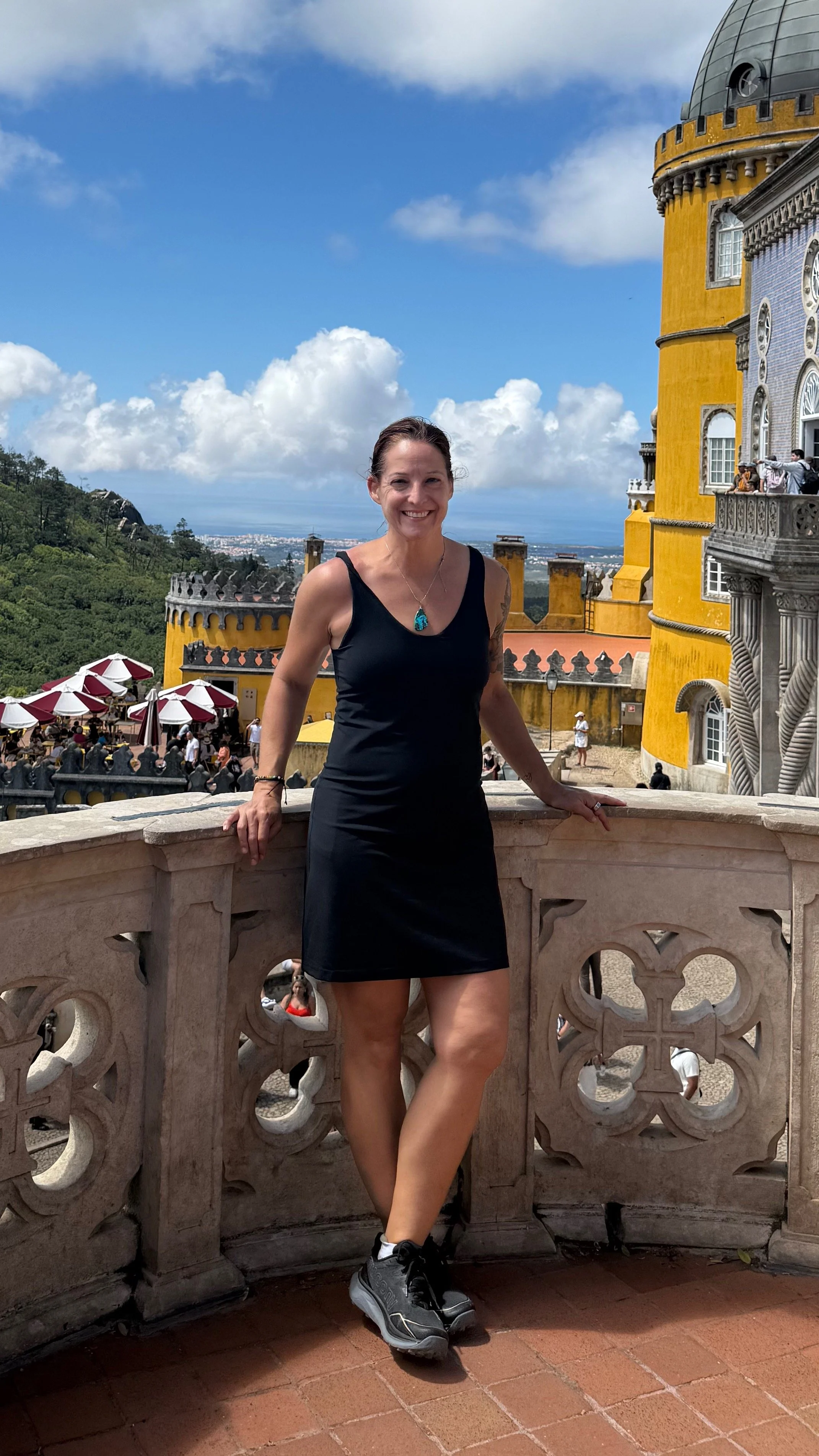 woman standing on a balcony at a large palace, with the vast sky and ocean behind her