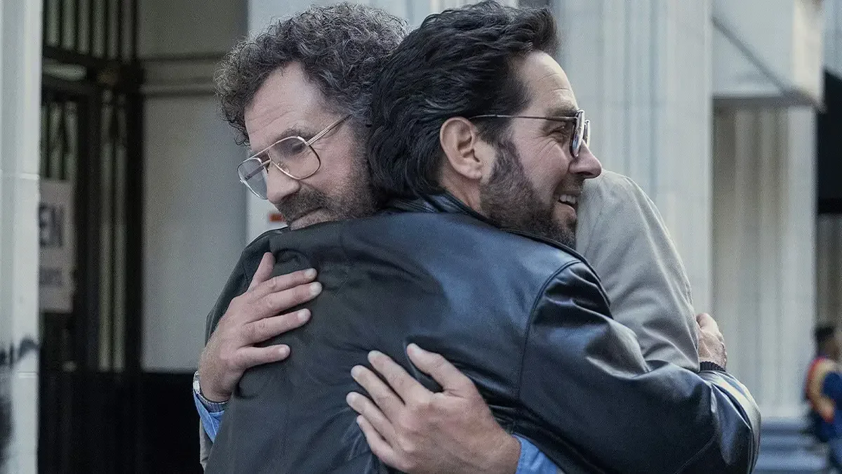 Will Ferrell and Paul Rudd hugging tightly while wearing 1980s-style glasses and beards.