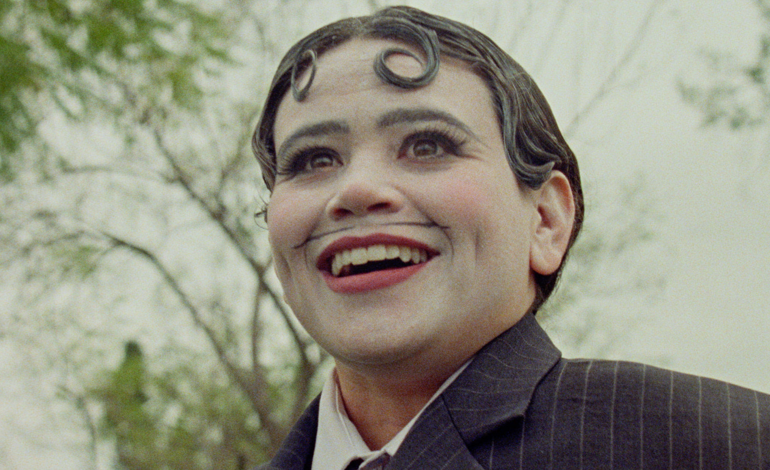 Close-up of a smiling performer in white face makeup, painted mustache, and a pinstripe suit in The Weird Guy.