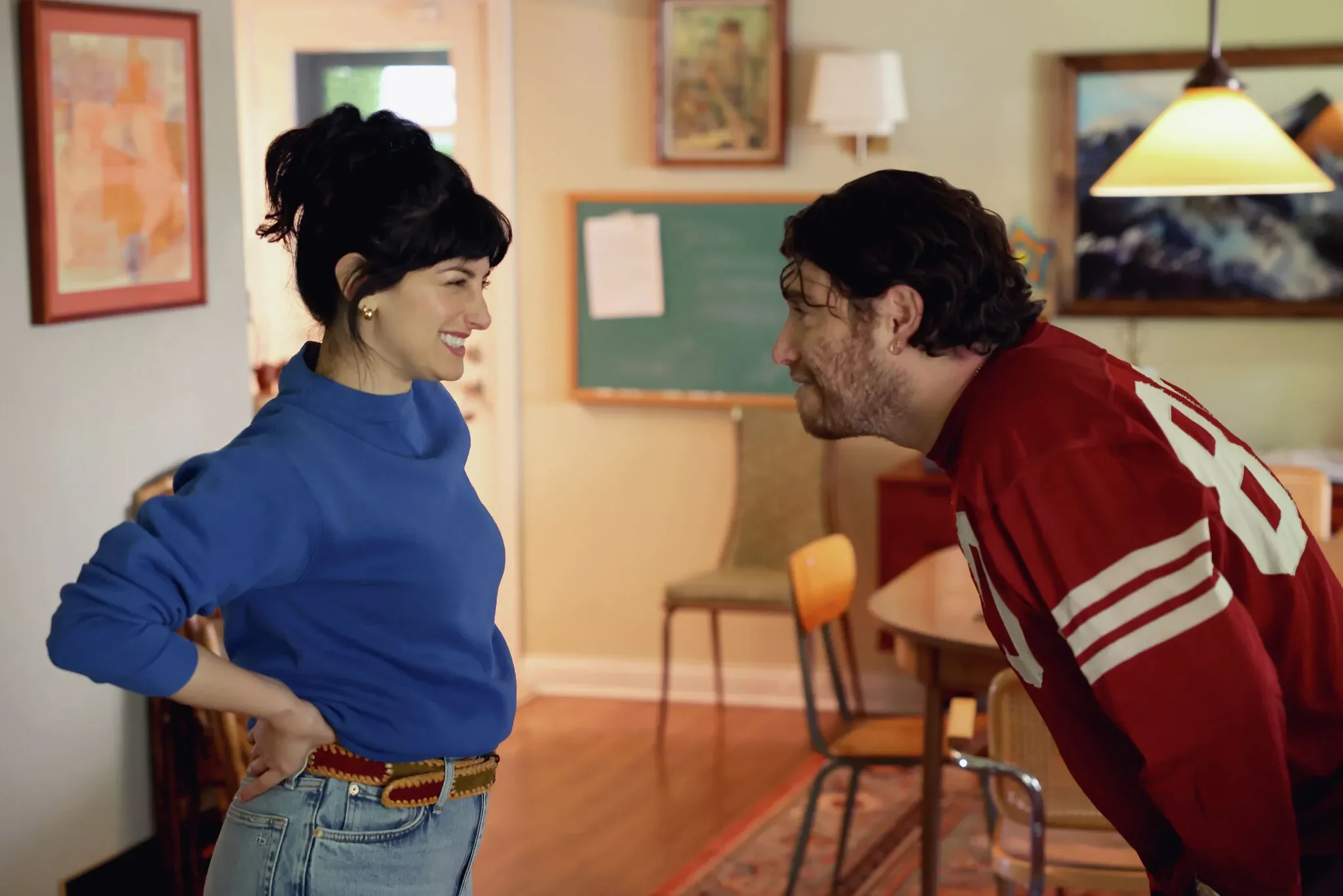 Ayden Mayeri in a blue turtleneck smiling at Adam Pally wearing a red sports jersey.