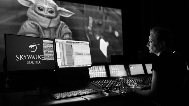 Sound engineer working at a mixing desk with Grogu from The Mandalorian displayed on the theater screen.
