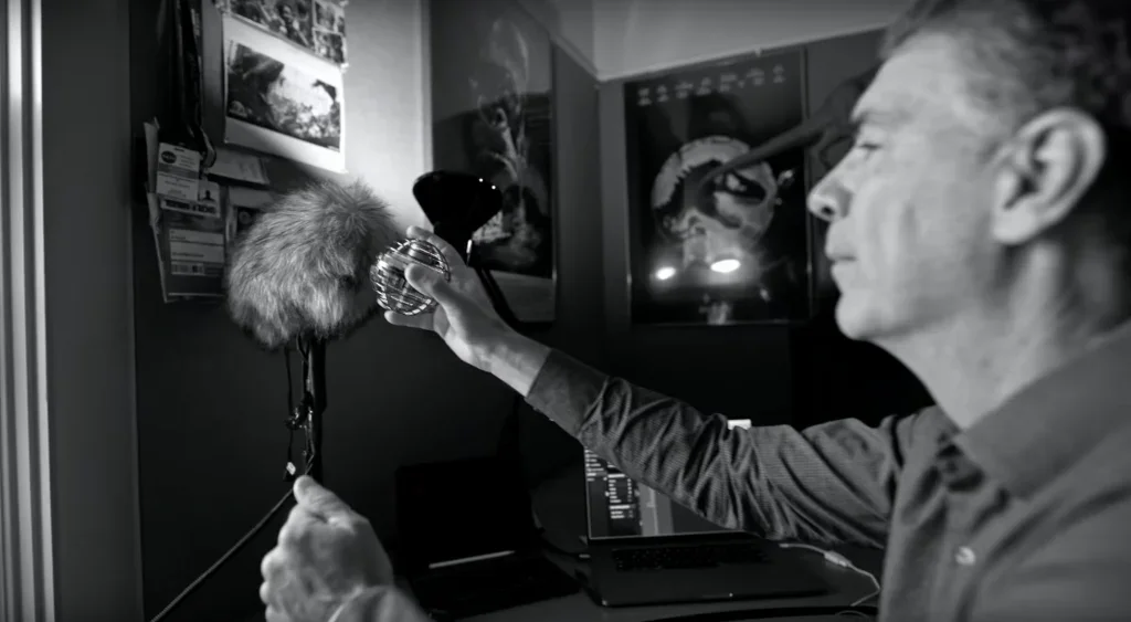 Sound designer holding a metal sphere prop near a microphone inside a sound studio.