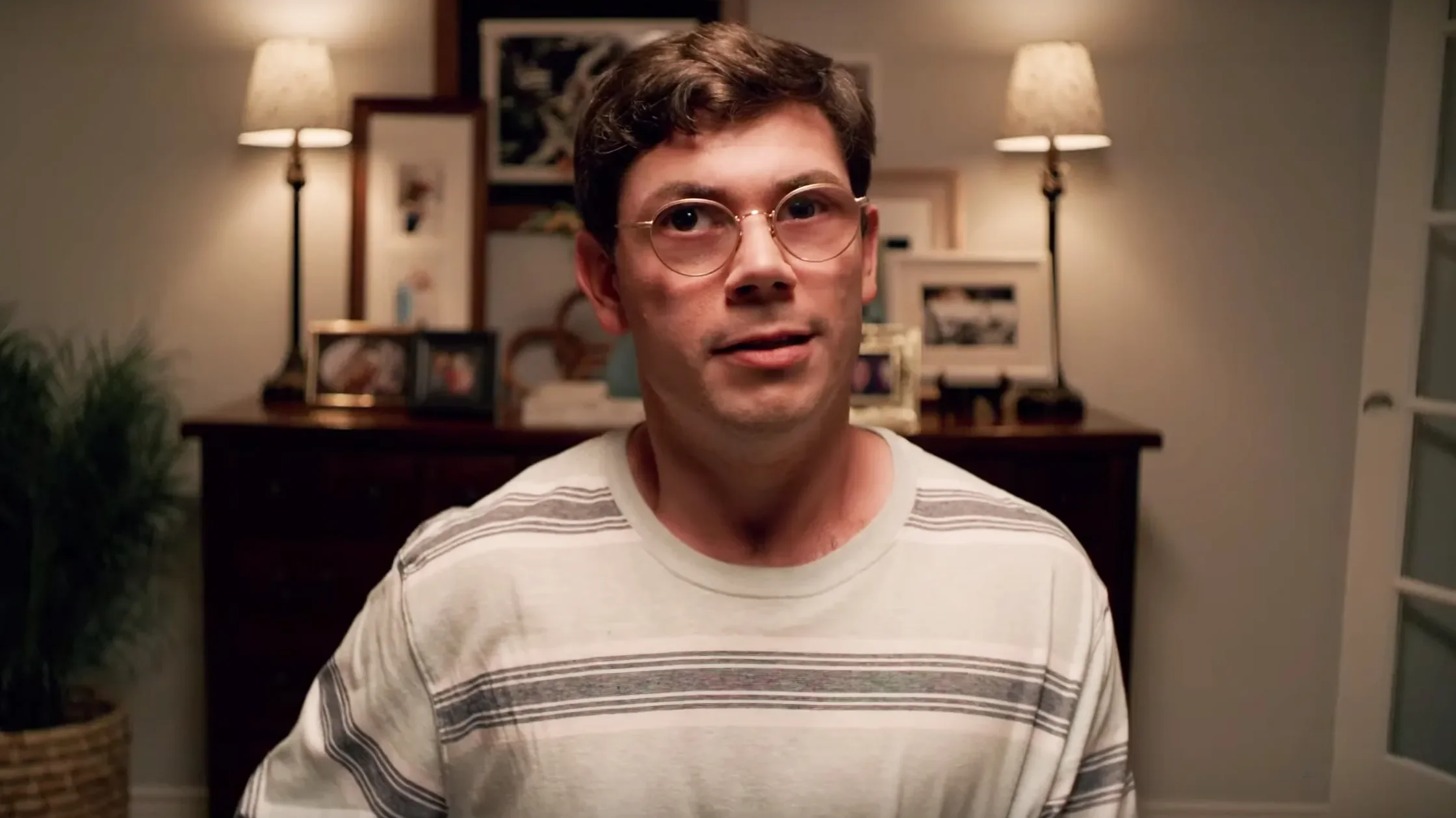 Ryan O'Connell wearing round wire-rimmed glasses and a striped shirt looking thoughtfully ahead.