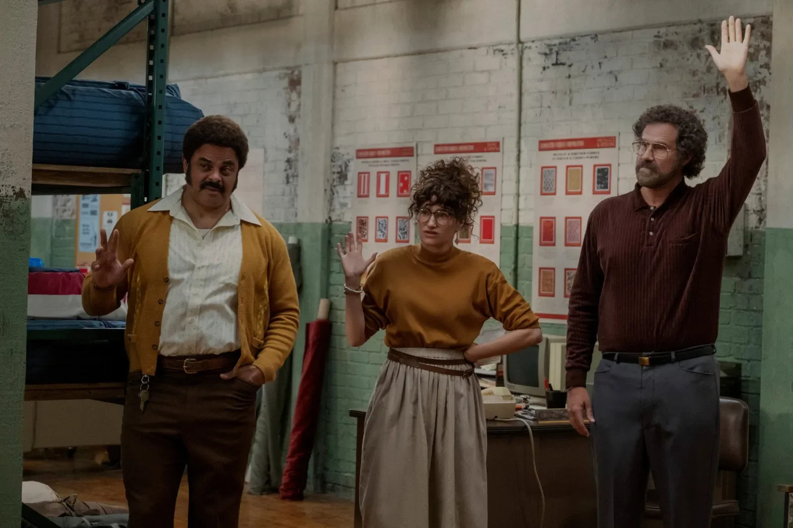 Will Ferrell raising his hand while standing next to two colleagues in a workshop.