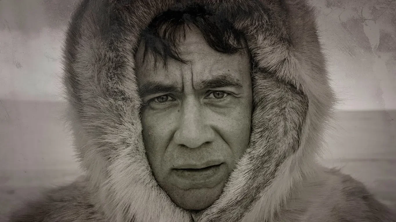 Black-and-white close-up portrait of Fred Armisen wearing a heavy fur-lined parka hood.