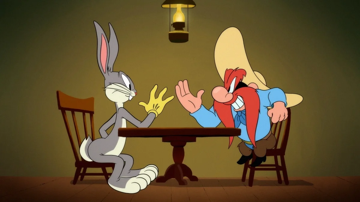 Bugs Bunny sitting across a wooden table from an angry Yosemite Sam under a hanging lamp.