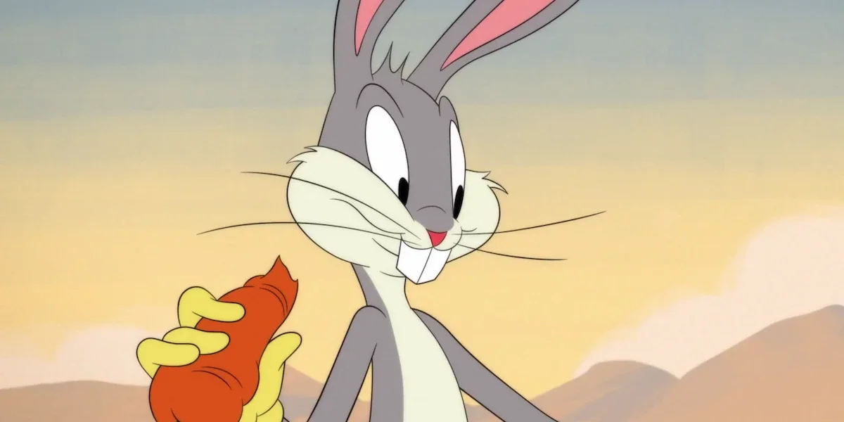 Close-up of Bugs Bunny smiling while holding a partially eaten carrot against a sunset sky.