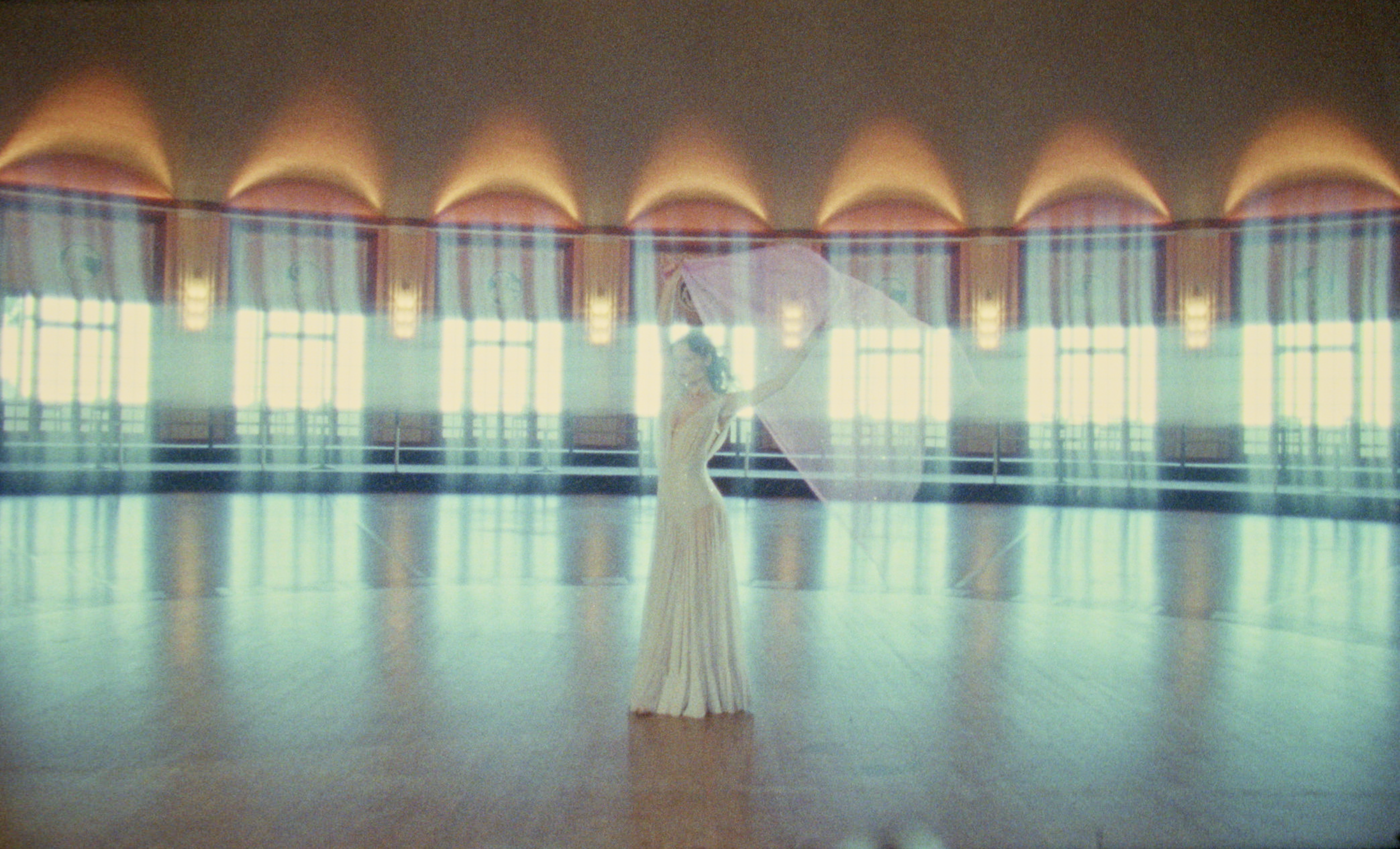 A woman in a white gown and flowing veil standing in the center of a grand Art Deco hall in The Weird Guy.