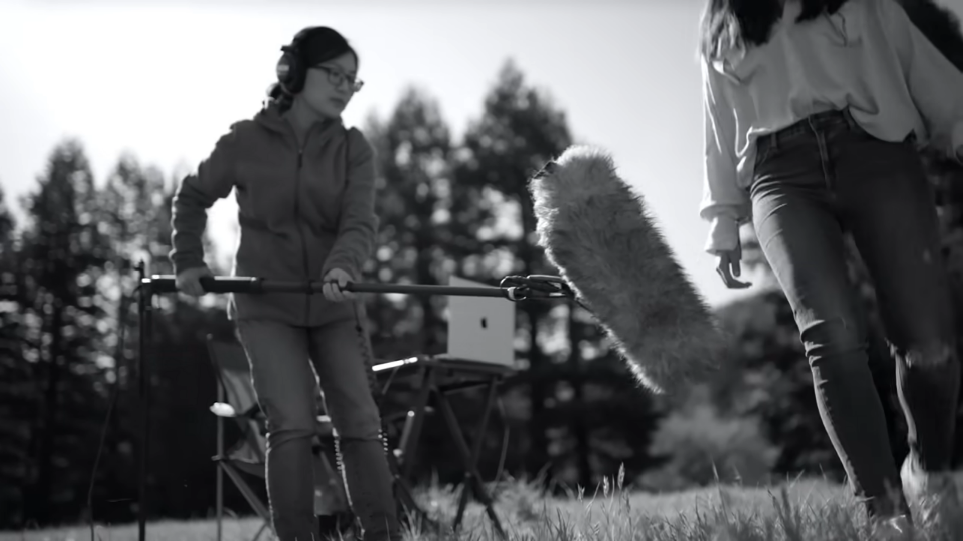 A sound engineer holding a boom microphone outdoors during a field audio recording session.