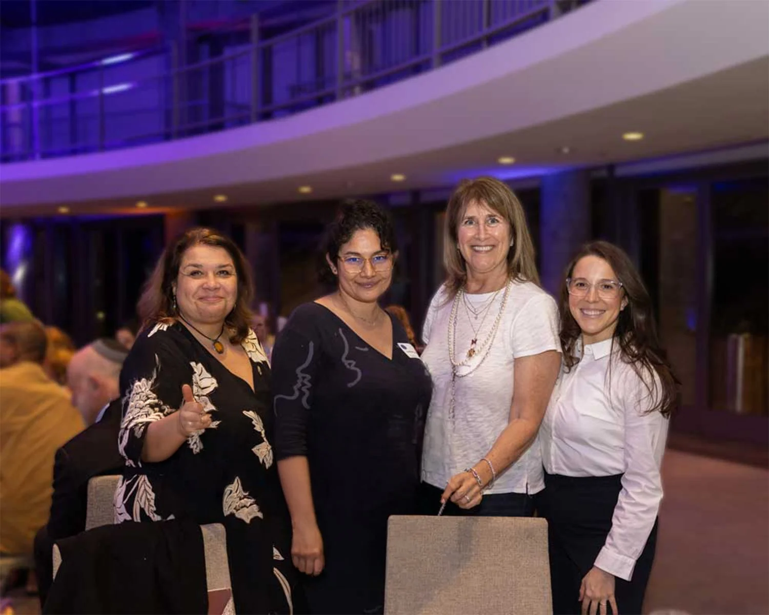 Four women standing together at an indoor event, smiling and posing for the camera.