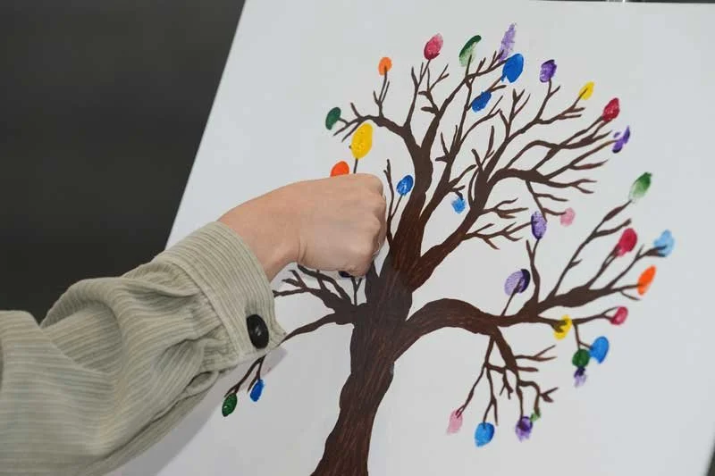 Woman's hand making a thumb print on a painted tree with brown branches.