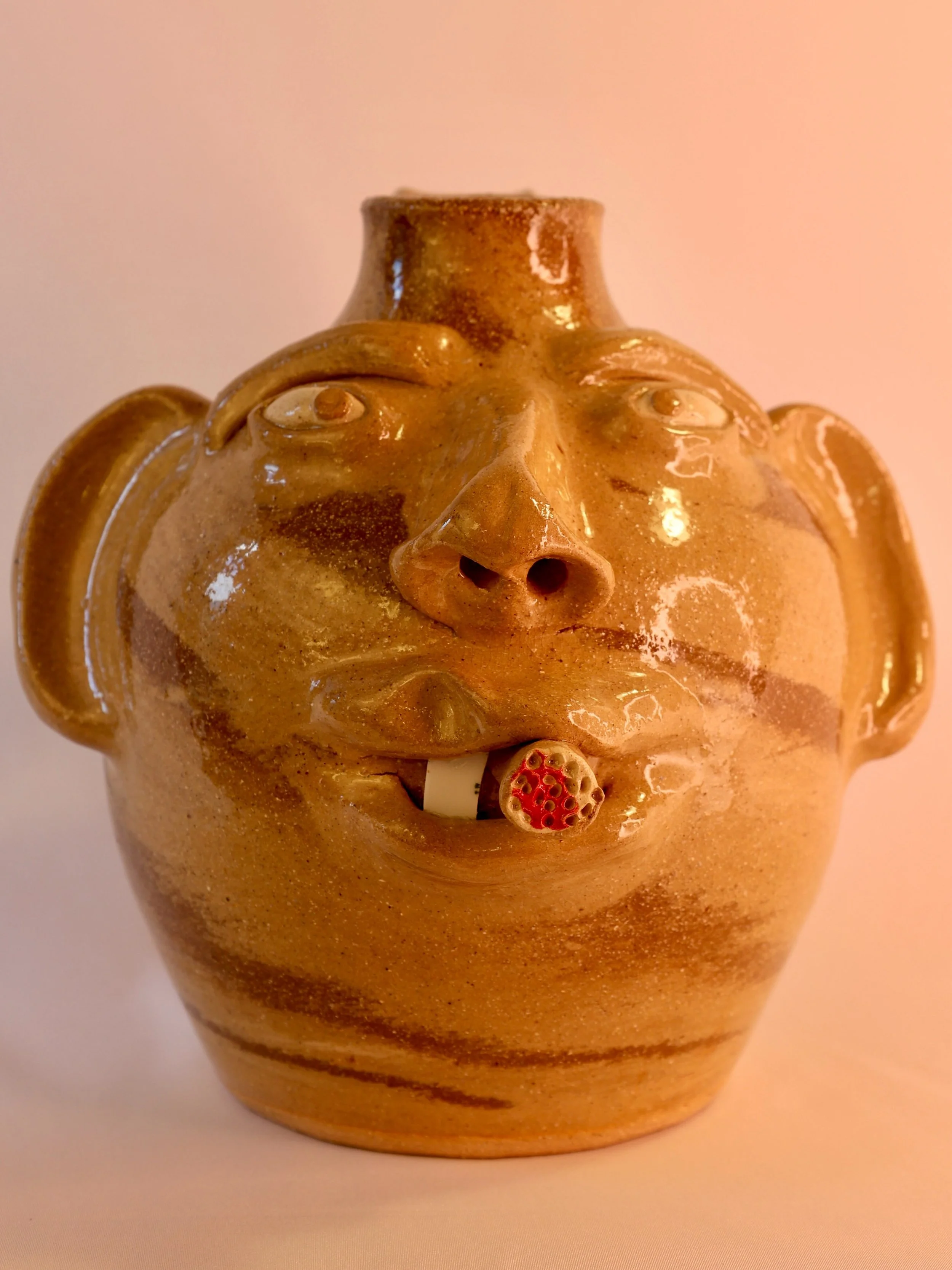School picture day for this face jug! This piece came to life at 2:14AM in 2021 at the hands of Dale Costner in Vale, NC according to the bottom of him. He&rsquo;s got a cigar hanging out of his mouth, a prominent sculpted nose, one tooth and a pair 