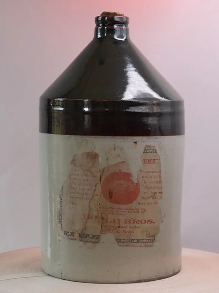 Captivated by this antique two-tone one-gallon stoneware jug, it is truly in outstanding condition. Void of chips and cracks, it features a mostly intact cork, and the original paper label, partially intact. Label text identifies its Lowell, Massachu