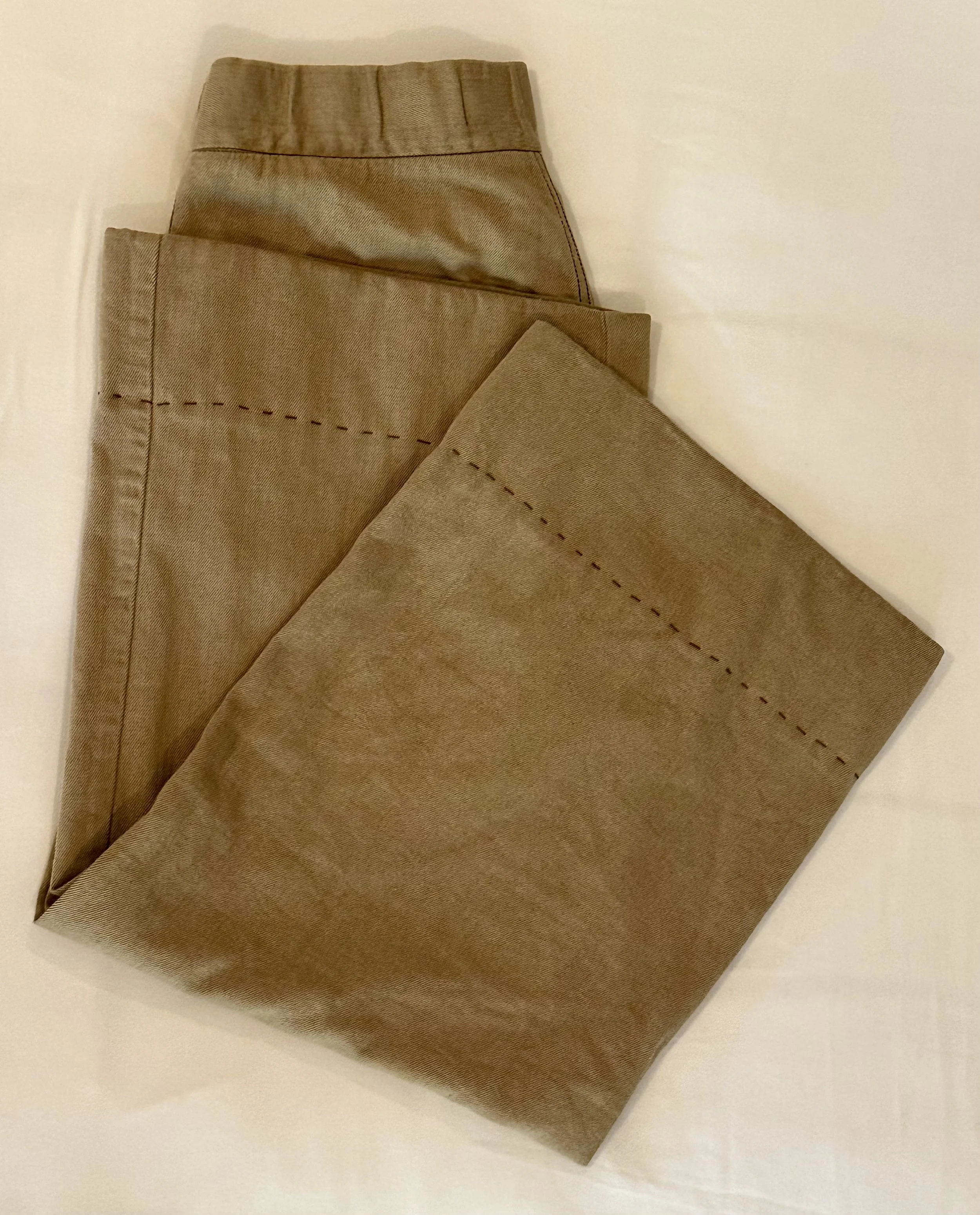 A pair of khaki-colored pants laid on a white surface.