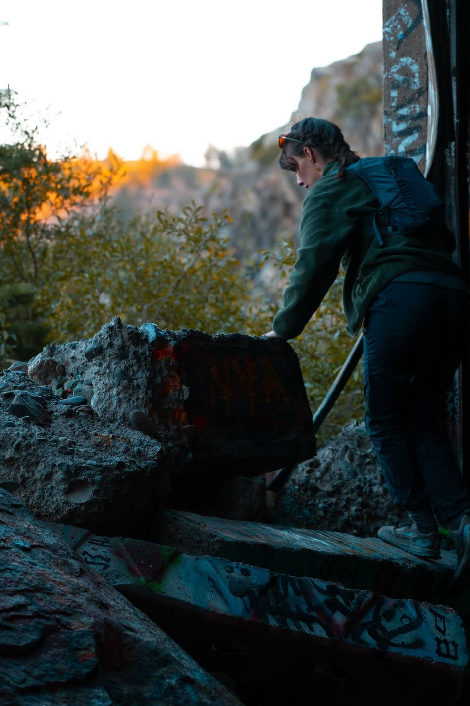 Person walking in a graffiti-covered tunnel in a rustic outdoor setting during sunset.
