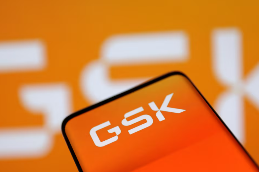 Close-up of a smartphone screen displaying the brand name 'GSK' with a blurred orange background containing white text.