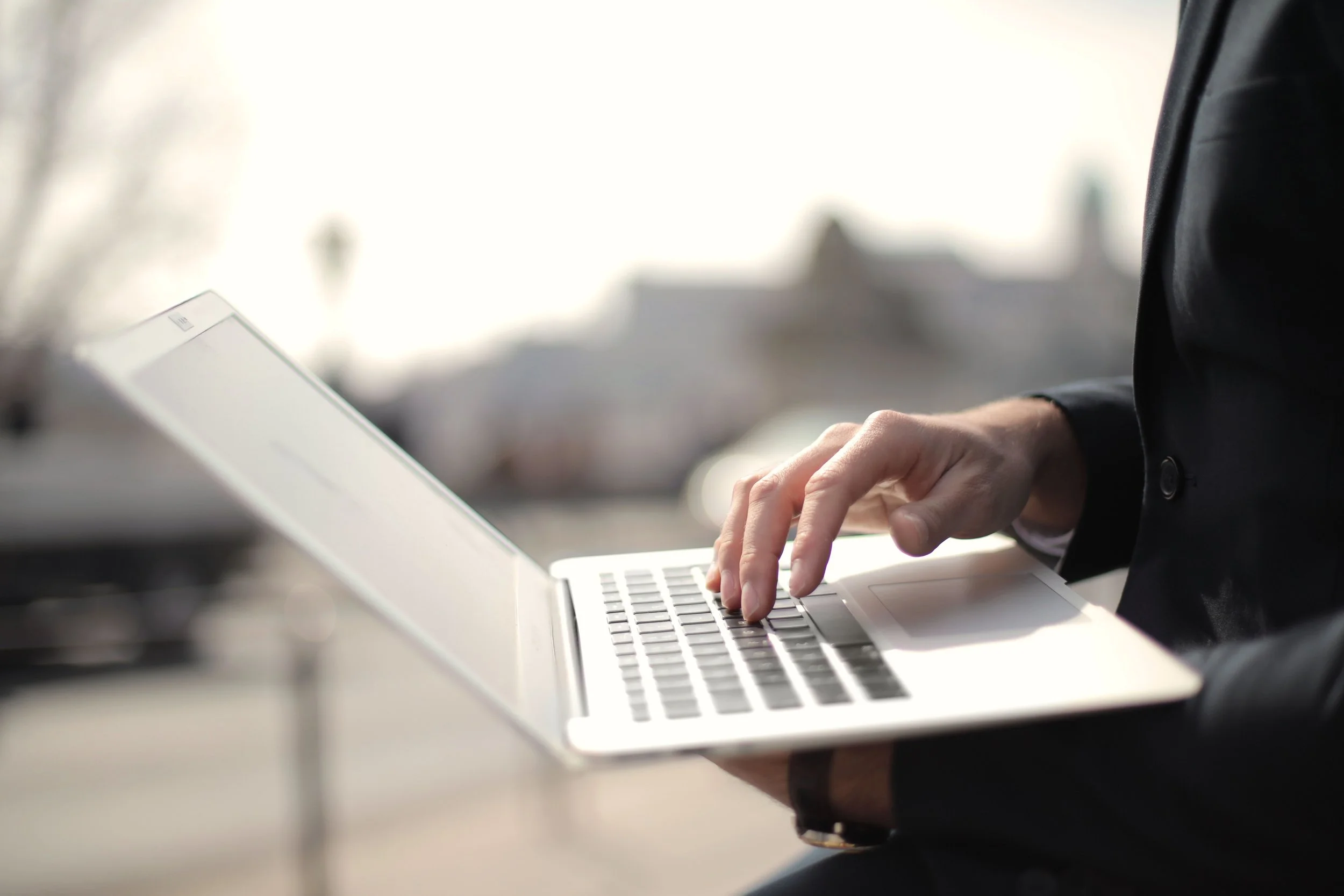 A person wearing a dark suit and white shirt typing on a laptop keyboard.