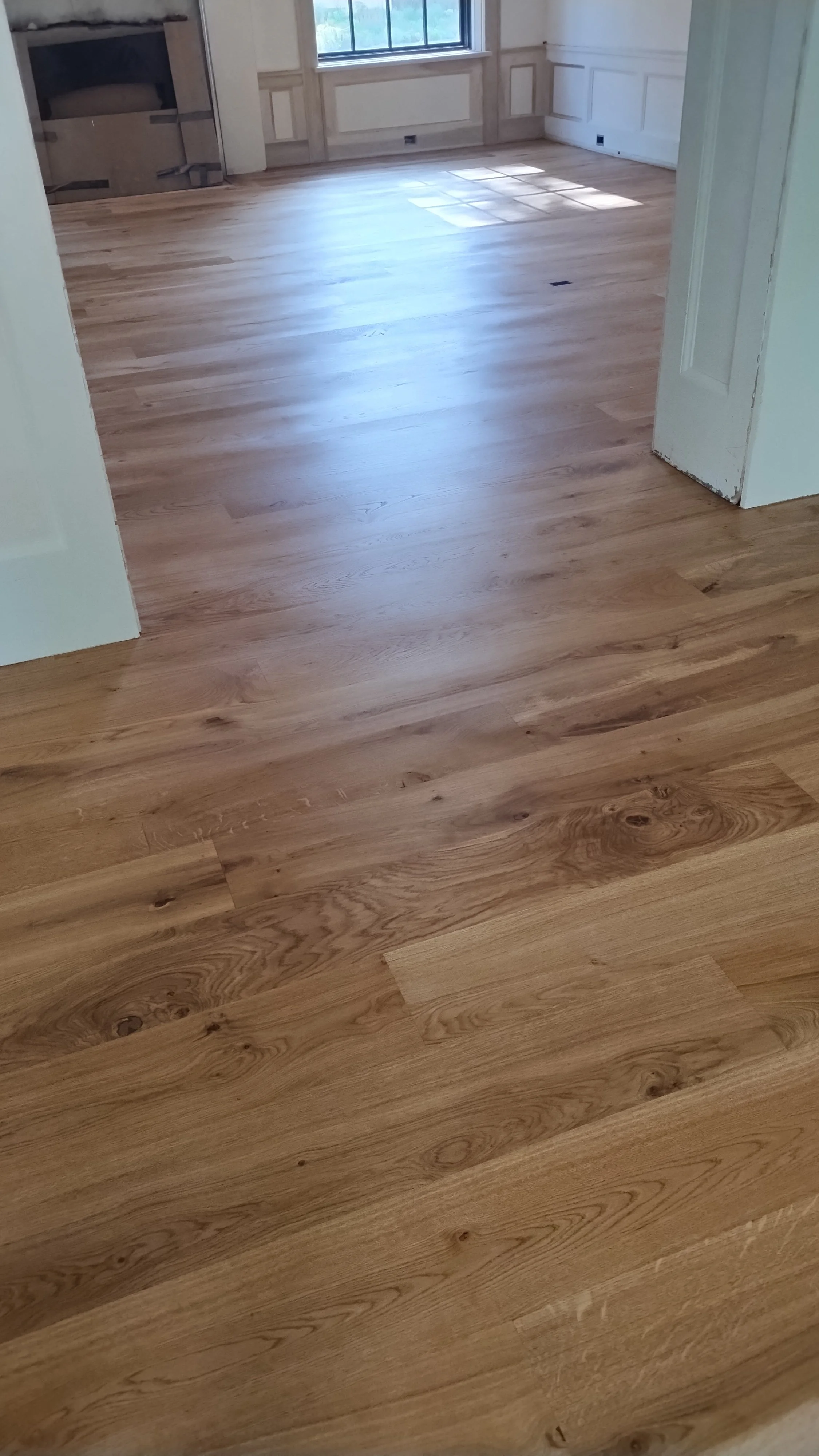 Photo of a room with newly installed hardwood flooring, white walls with molding, and a window letting in natural light.