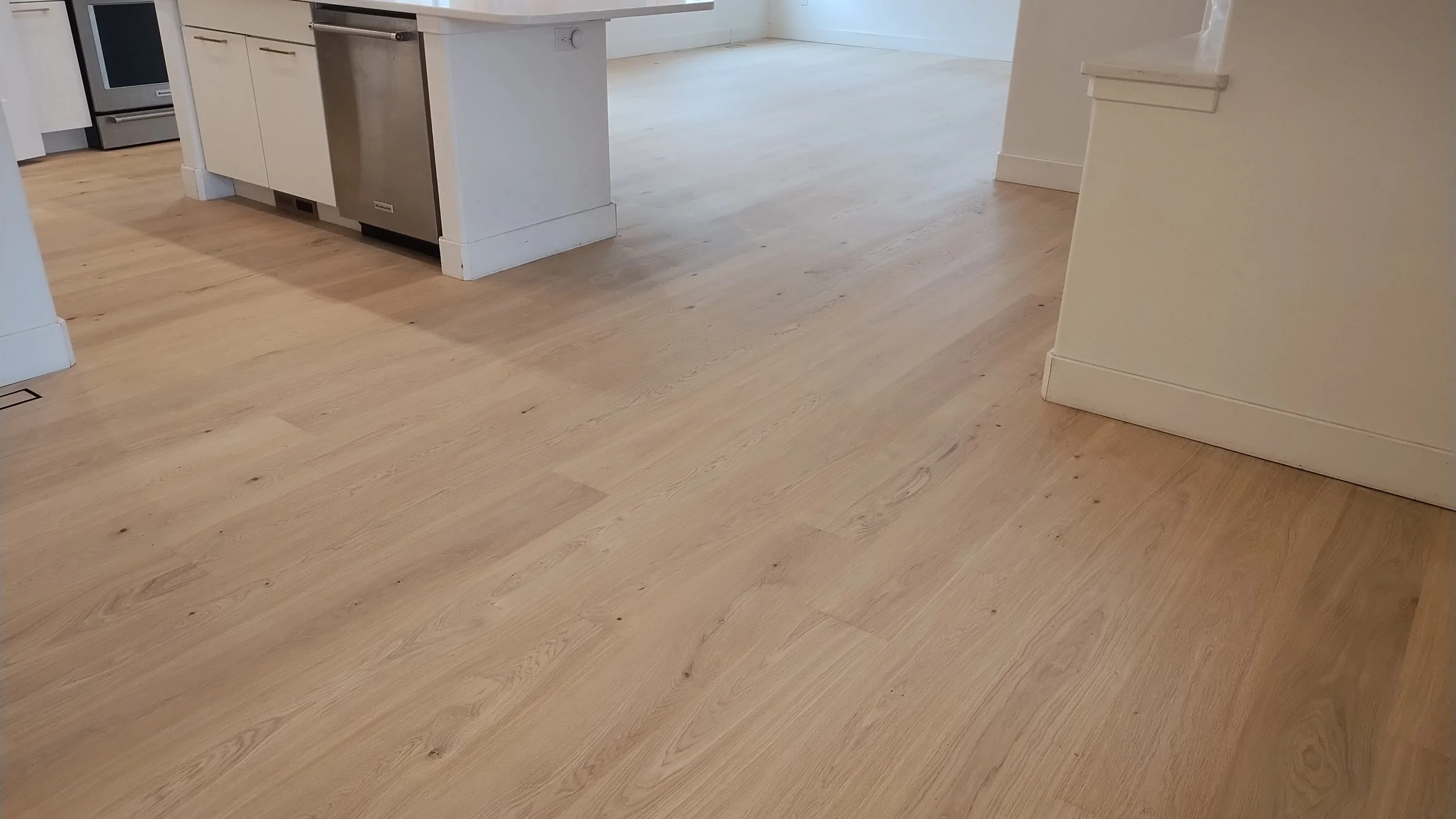 A corner of a kitchen with light hardwood flooring, white cabinetry, and stainless steel appliances.