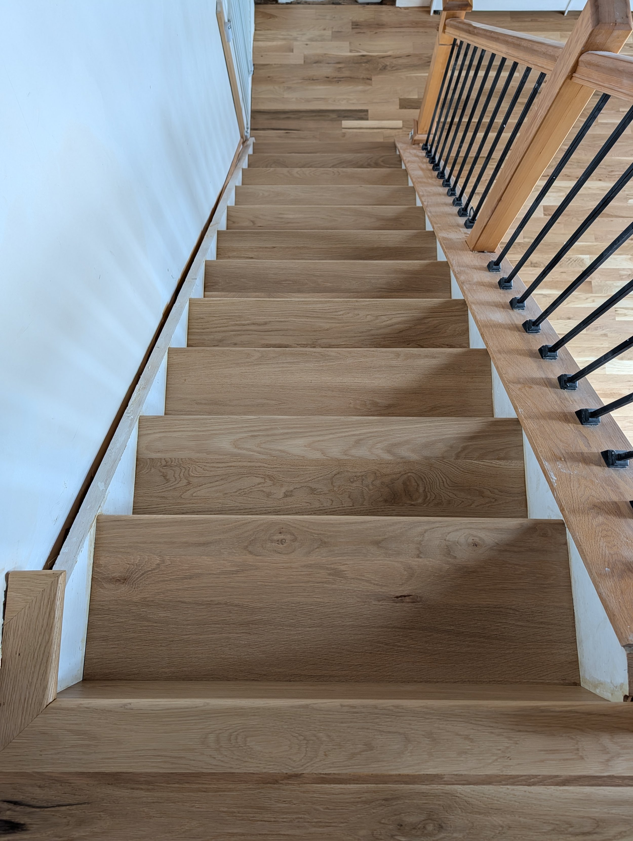 Wooden stairs with black metal railing leading down to a wooden floor.