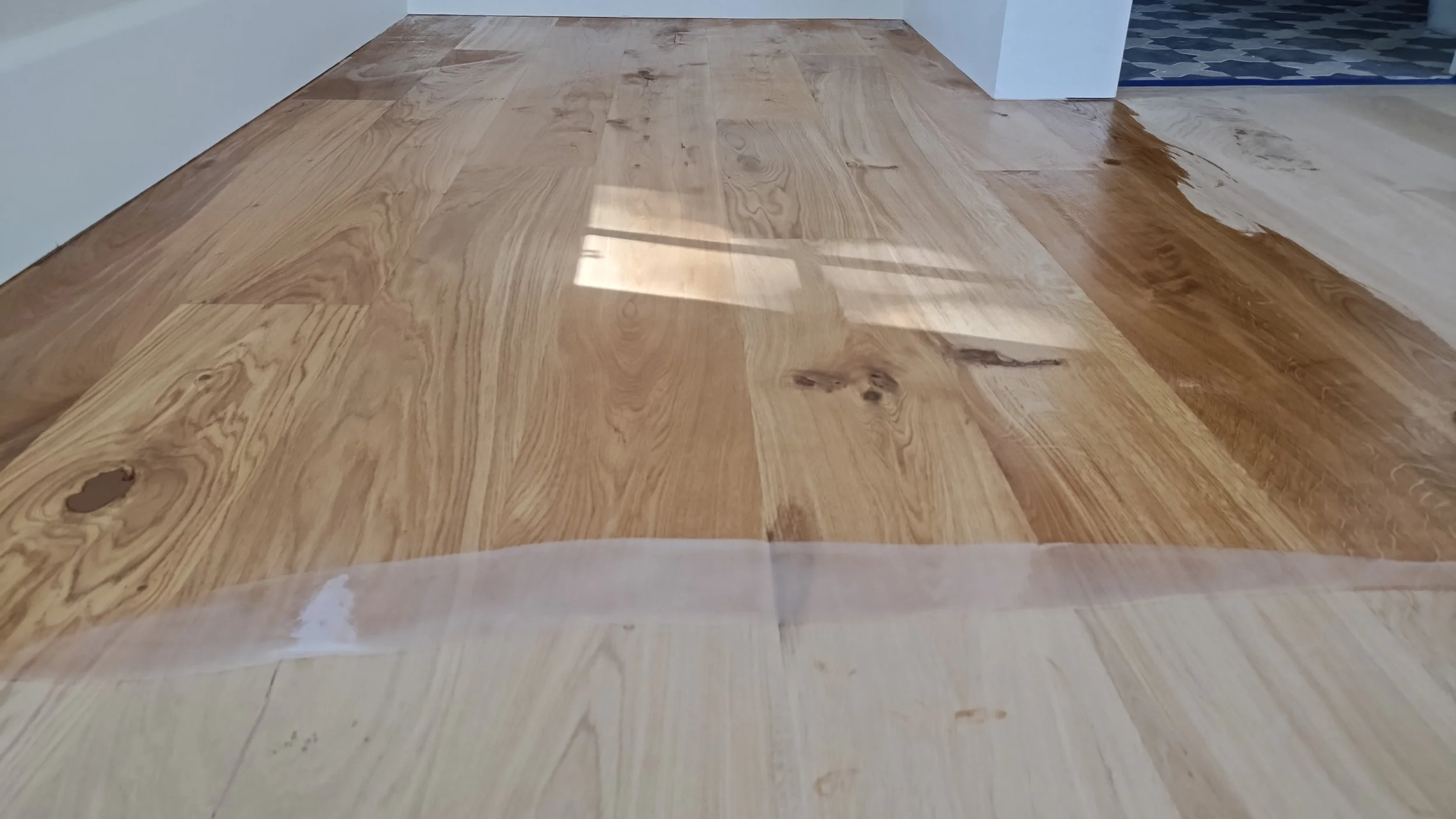 Close-up of a hardwood floor being refinished, with part of the floor coated in a shiny finish and the other part not yet finished.