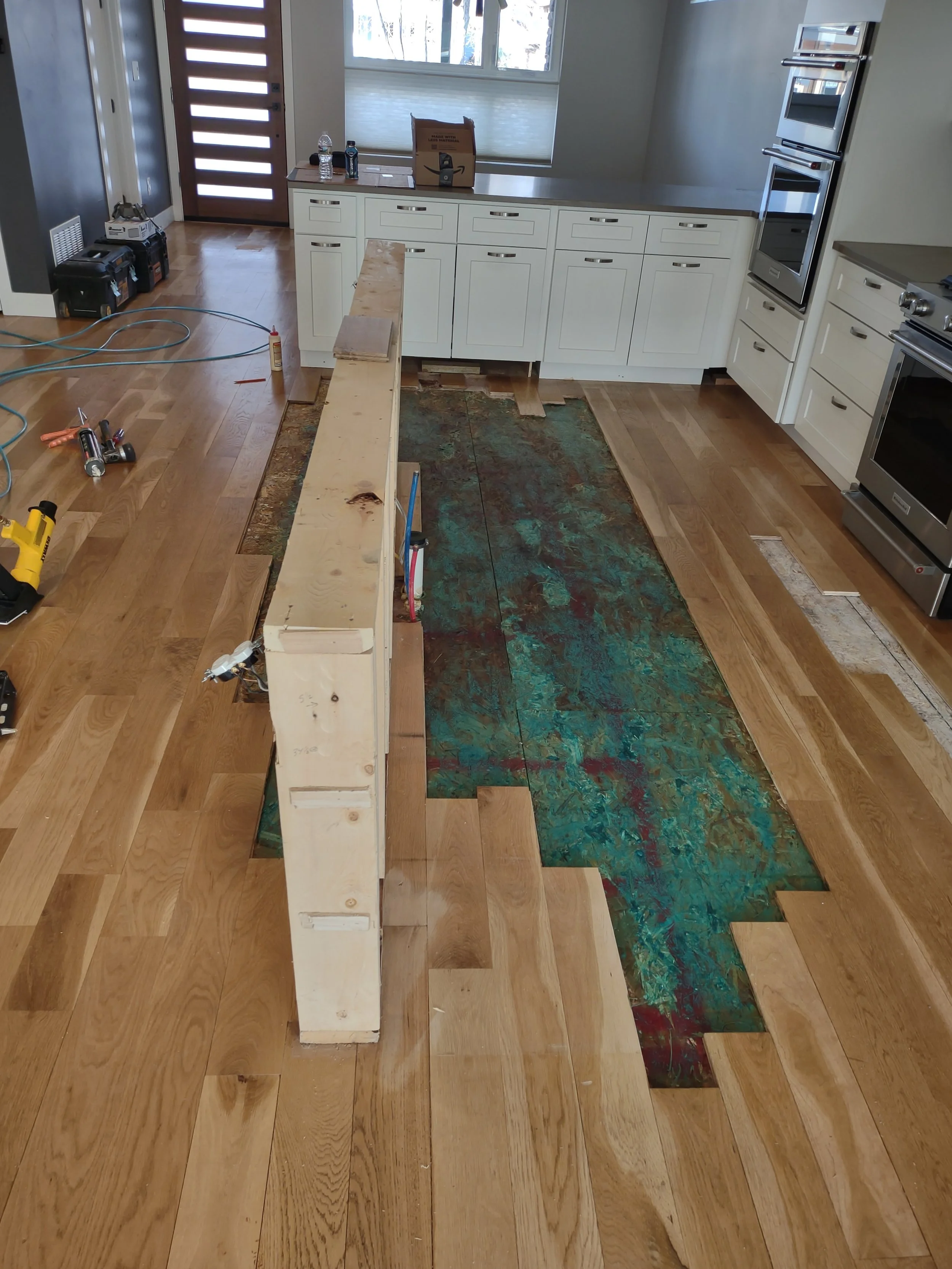 A kitchen under renovation with a partially removed central island, construction tools, and protective coverings on the floor.