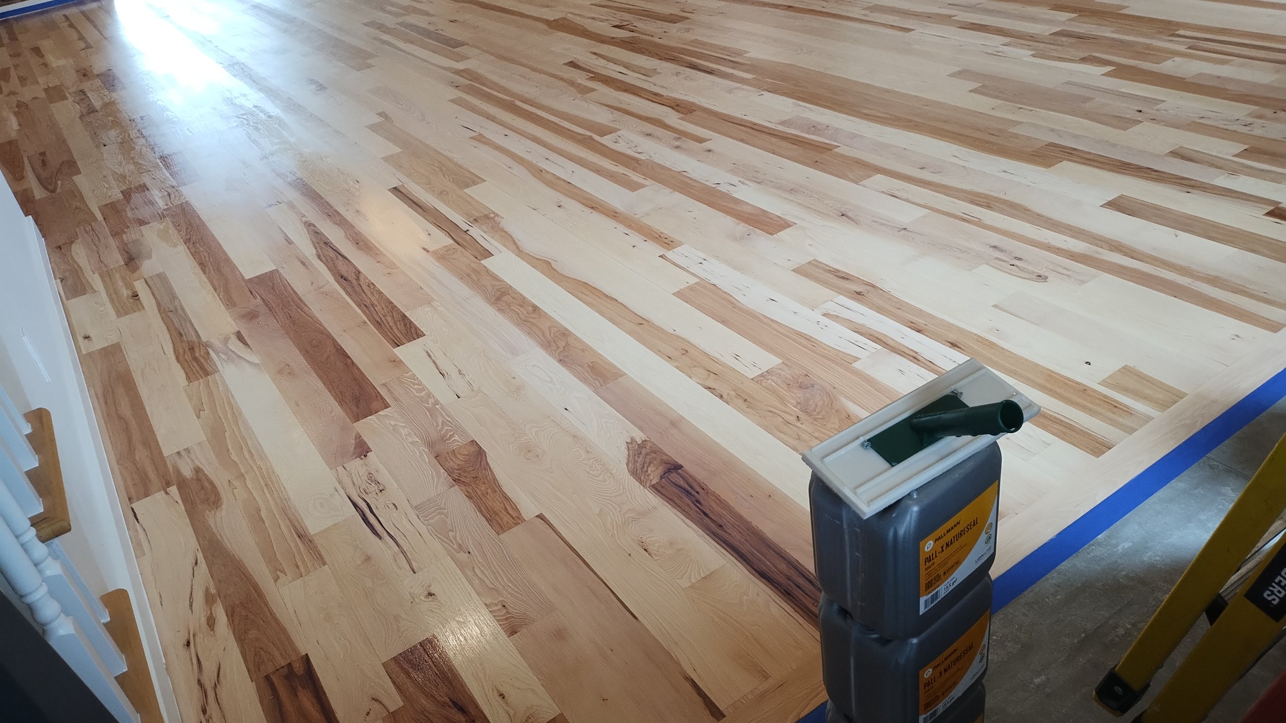 Newly installed hardwood flooring in a room, with a bucket of floor finish or stain nearby.