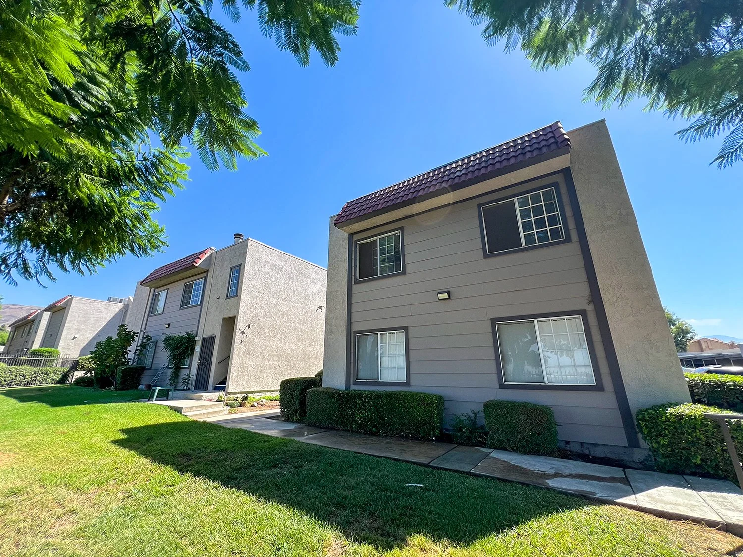 Cozy exterior of Highland Club Apartments with surrounded by large shade trees and lush grass.