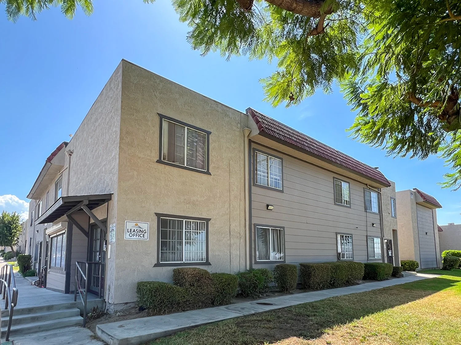 Cozy exterior of Highland Club Apartments with surrounded by large shade trees and lush grass.