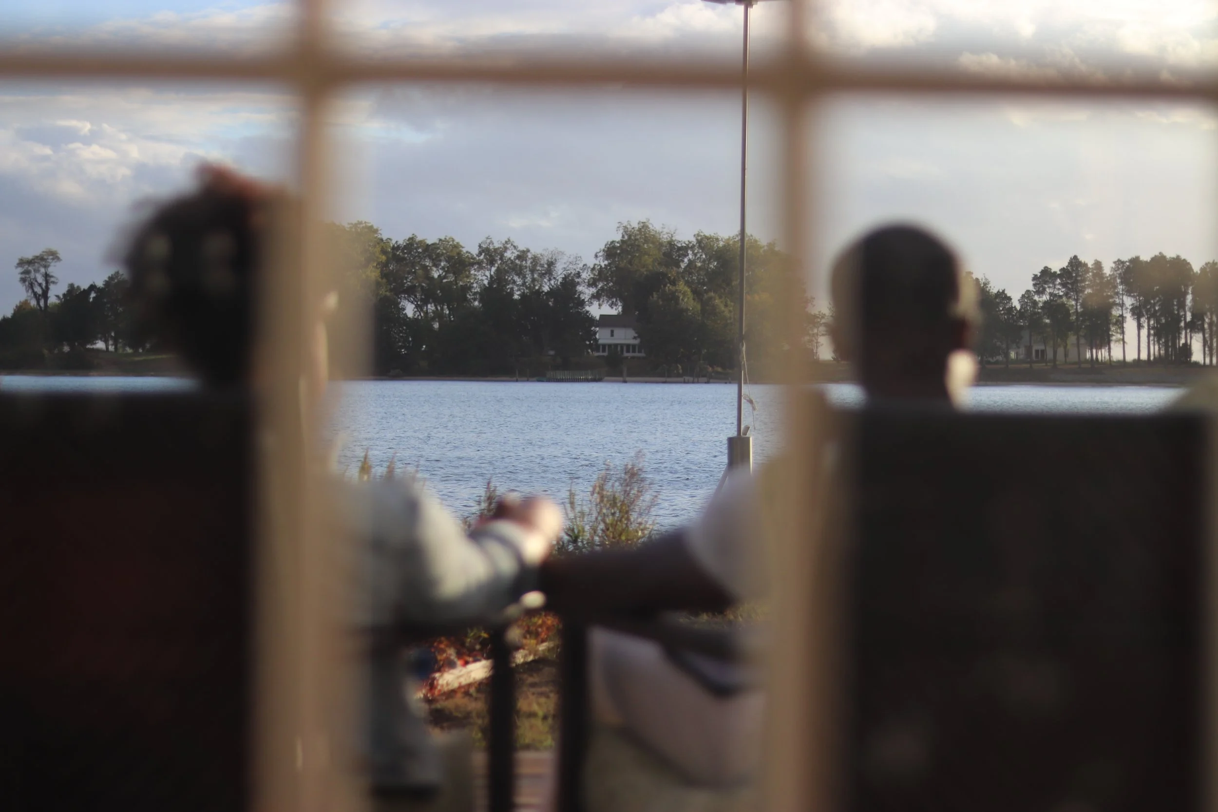 Couple sitting together on a lake house deck, during a quiet moment of reflection holding hands and looking out across the water.