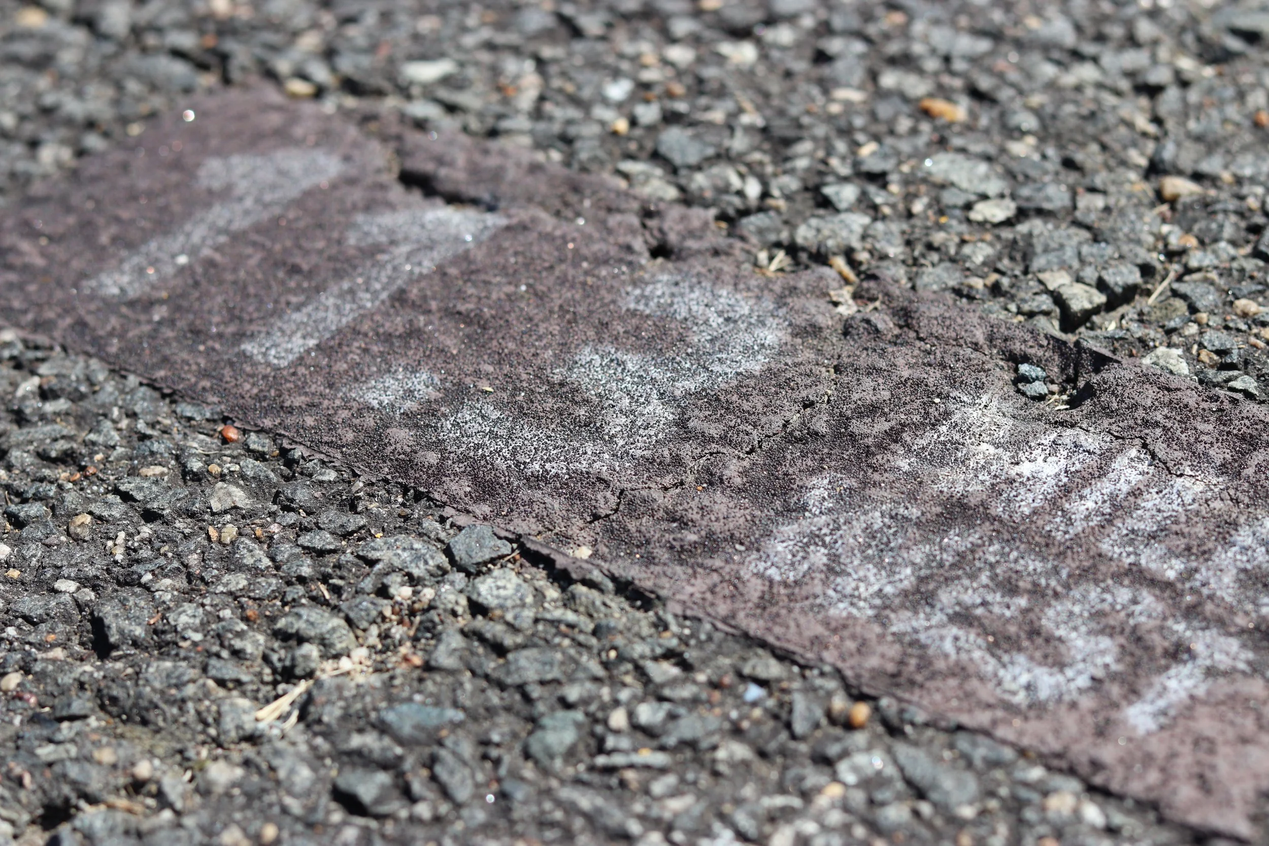 Close-up of asphalt pavement with chalk markings and small gravel scattered.