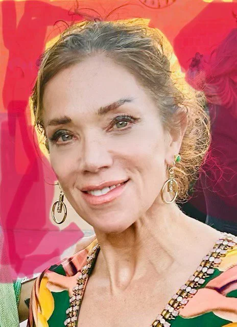 Close-up of a smiling woman with earrings and colorful clothing, outdoors with a pink background.