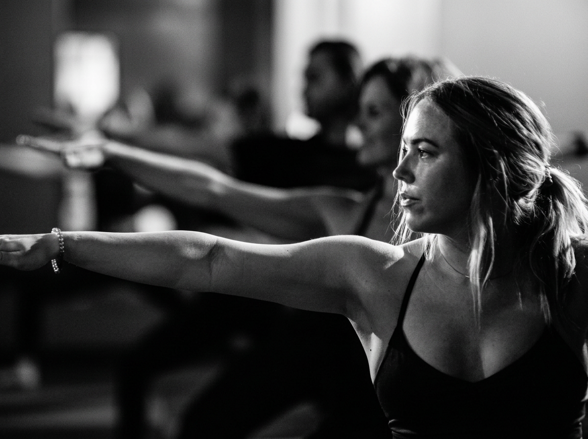 Women participating in a fitness class, extending their arms forward, focus on physical exercise, in a dimly lit room.