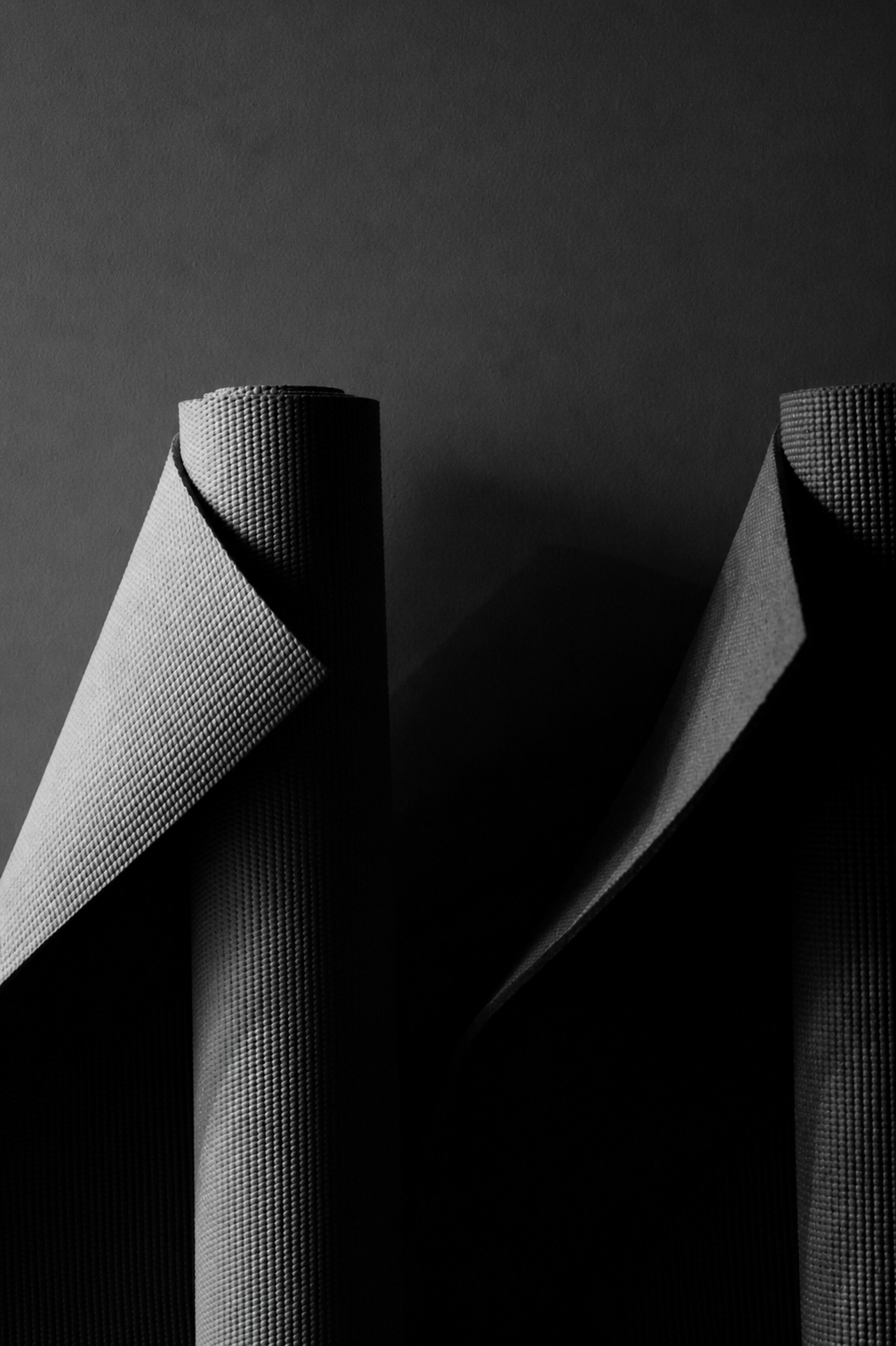 Close-up of two rolled-up yoga mats with textured surfaces, standing against a dark background, casting shadows.