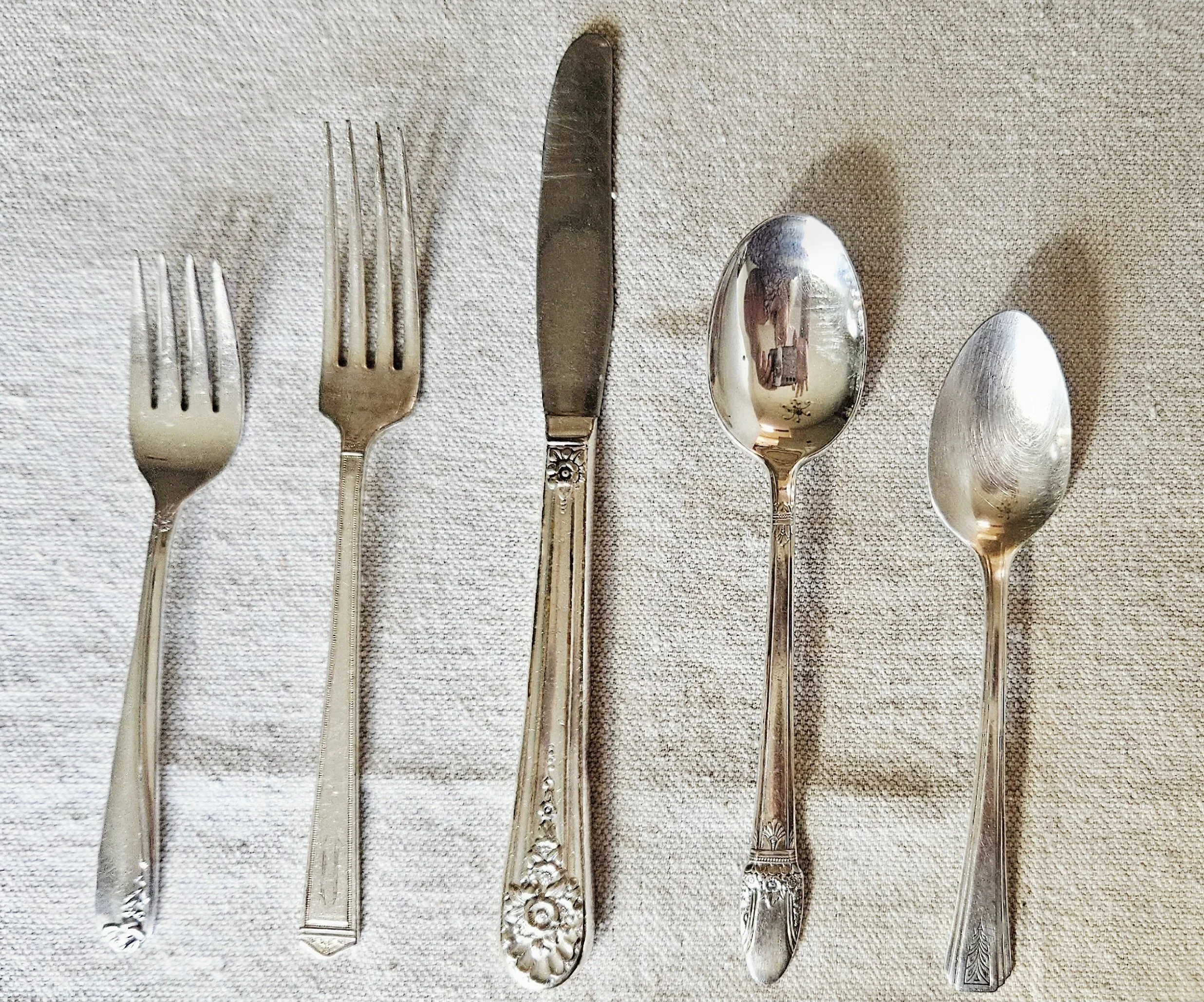 Set of four vintage silverware pieces, including two forks, one butter knife, and two spoons, laid out on a textured white cloth.