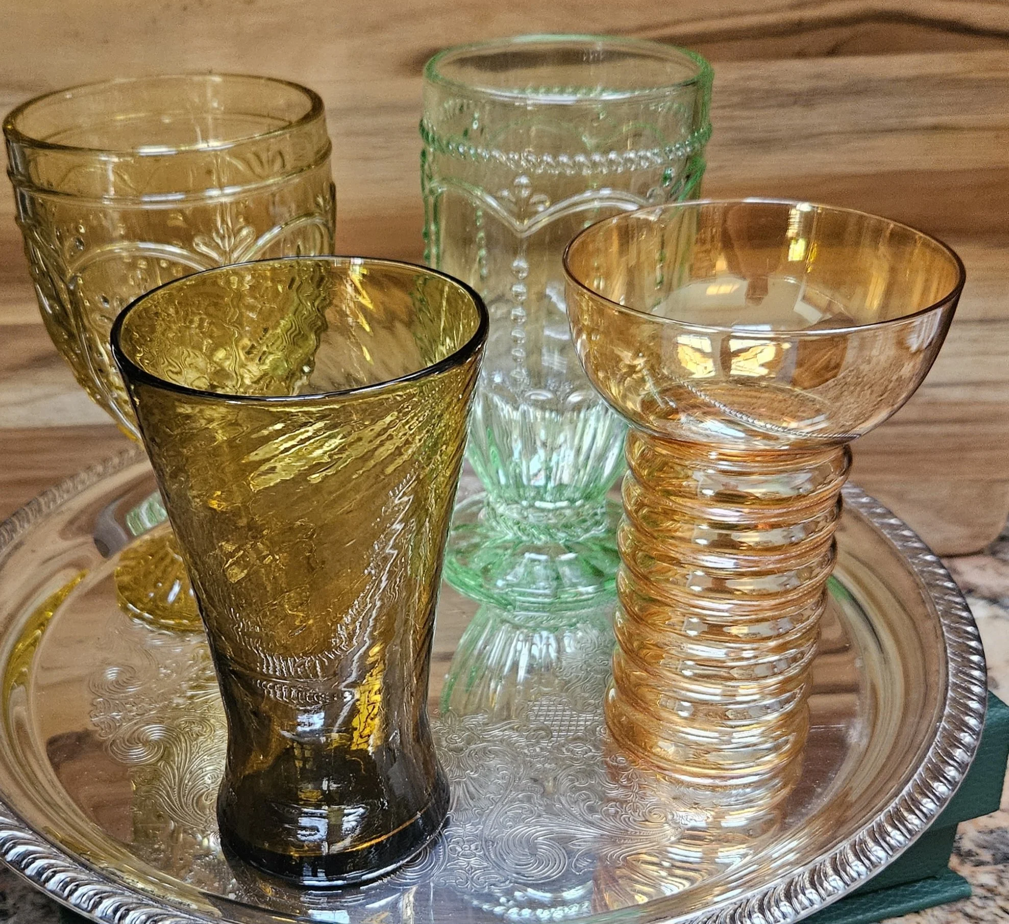 Set of five vintage glass tumblers with embossed patterns, various colors including clear, amber, and green, placed on a decorative glass tray with a silver rim.