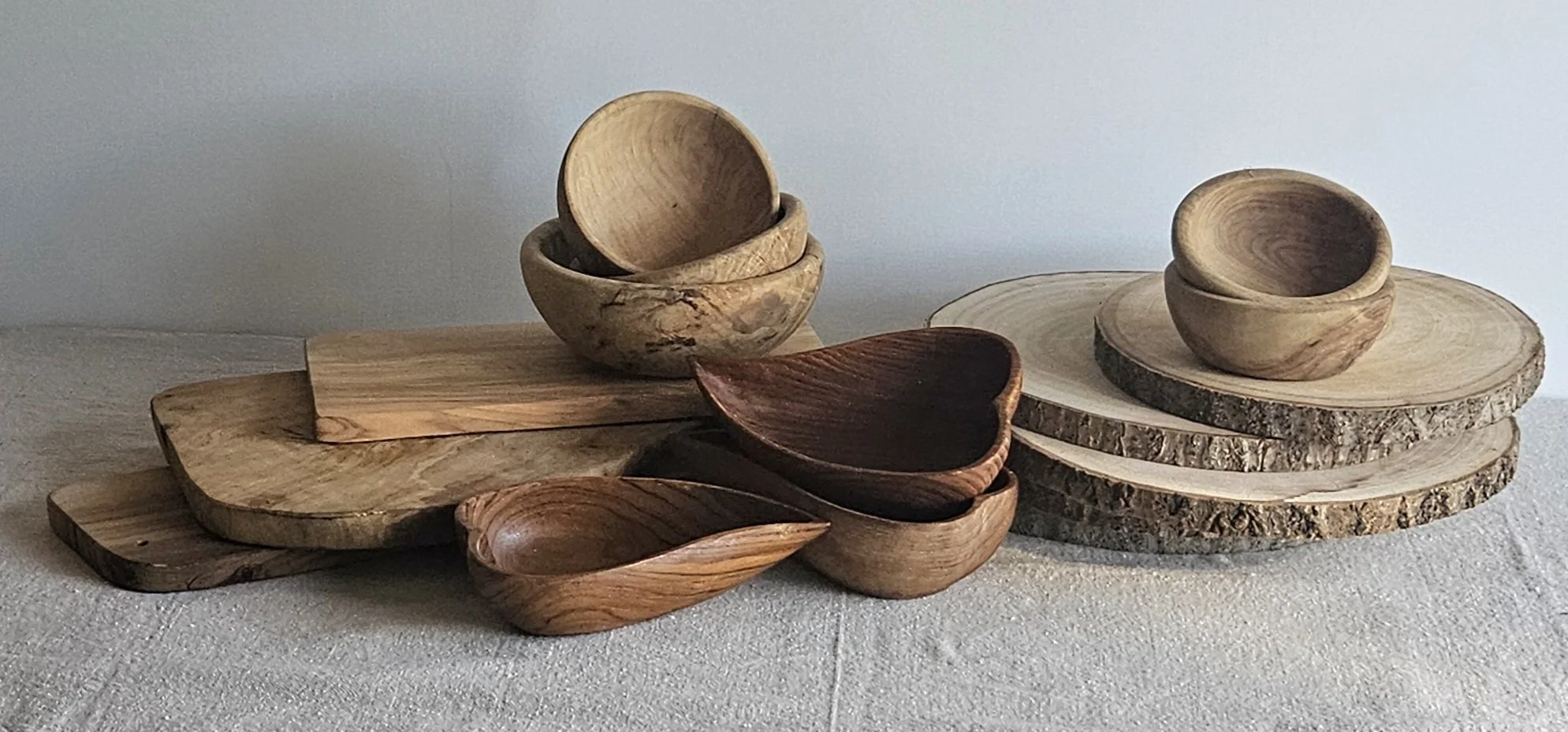 Various wooden bowls and plates arranged on a light-colored surface, with some stacked and others placed individually, against a plain background.