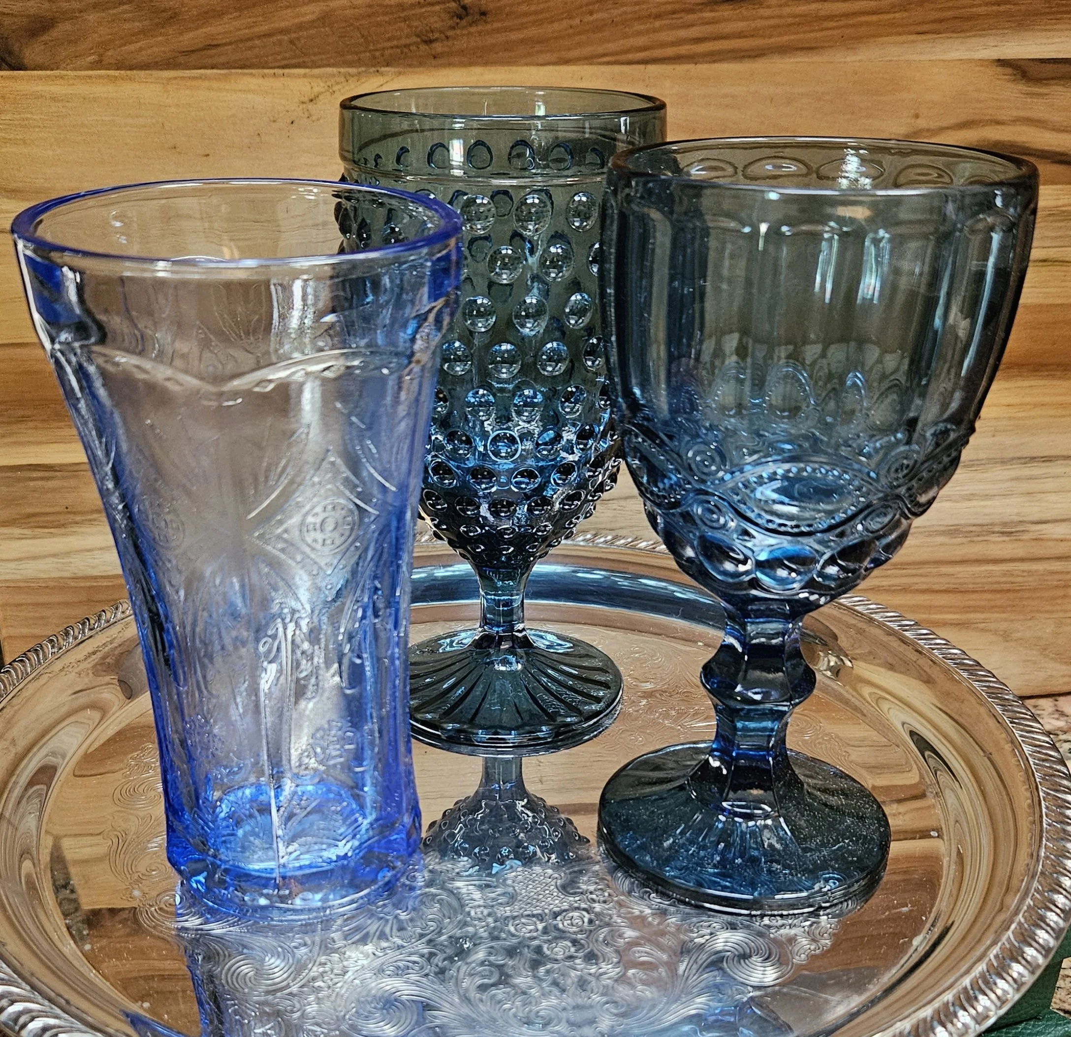 Four glass cups with textured surfaces, placed on a round wooden tray on a wooden surface.