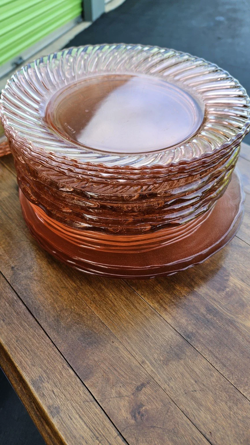 Stack of glass dinner plates with a raspberry tint, placed on a wooden table.