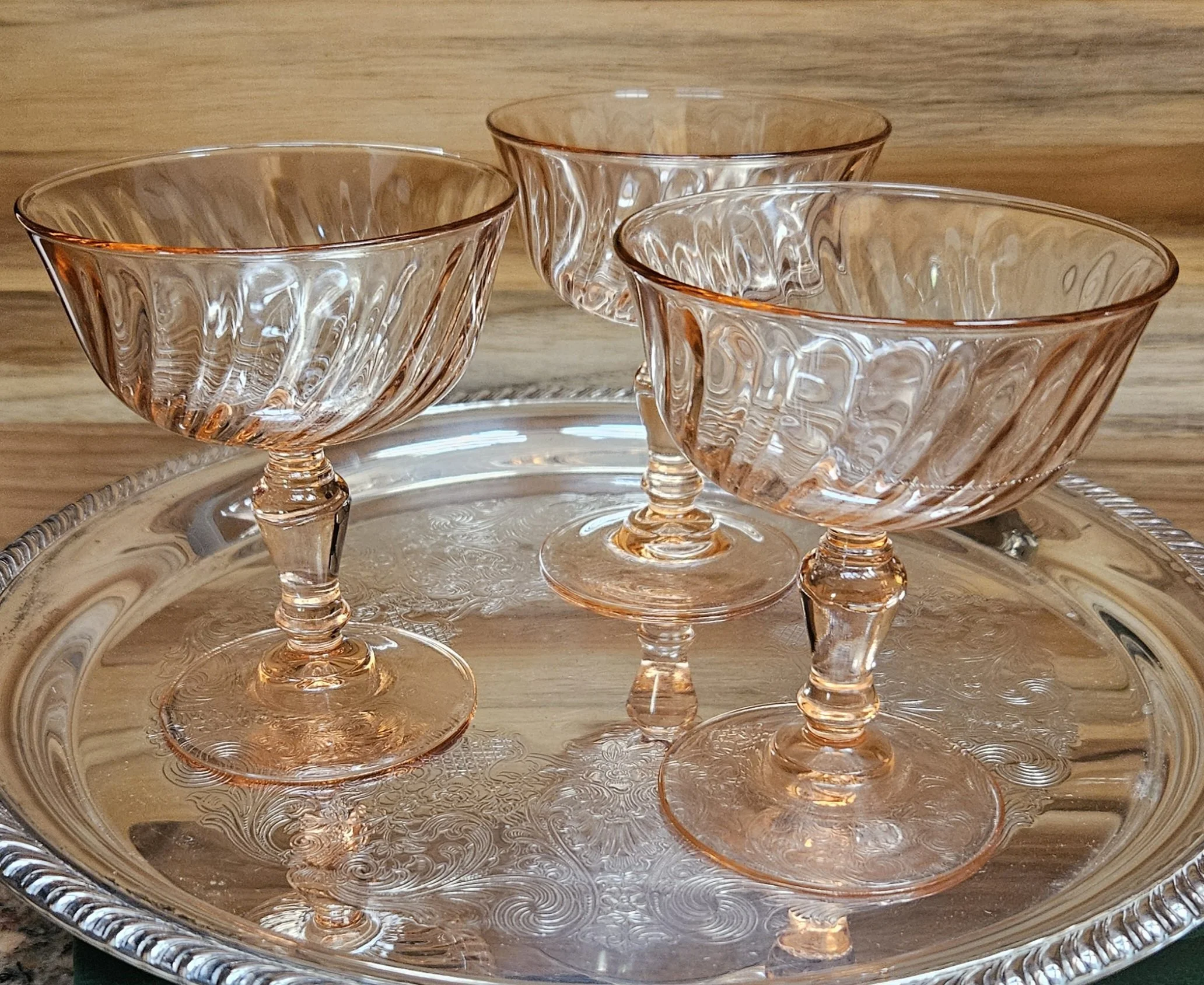 Four empty pink-tinted glass dessert cups with pedestal bases on a silver tray, placed on a wooden surface with a wooden background.