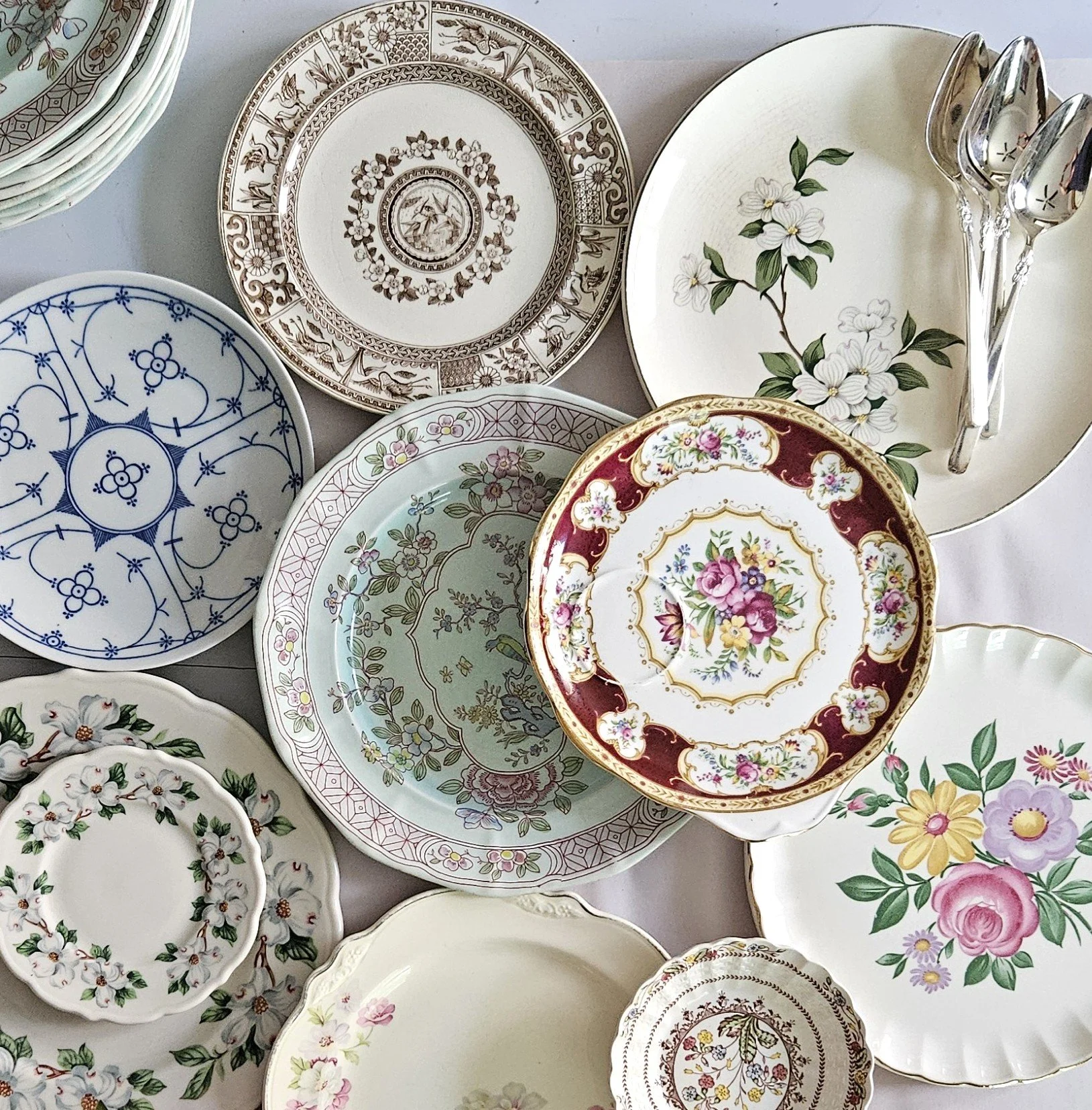 A collection of various decorative porcelain and ceramic plates with floral, geometric, and ornate patterns, arranged overlapping each other.