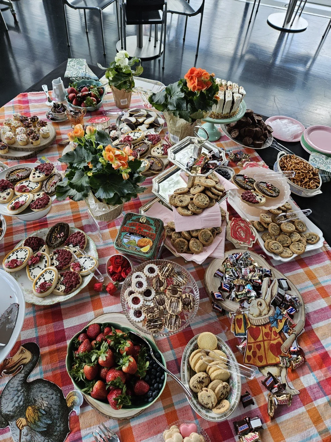 A table filled with various cookies, candies, strawberries, and decorative flower arrangements for a celebration or party.
