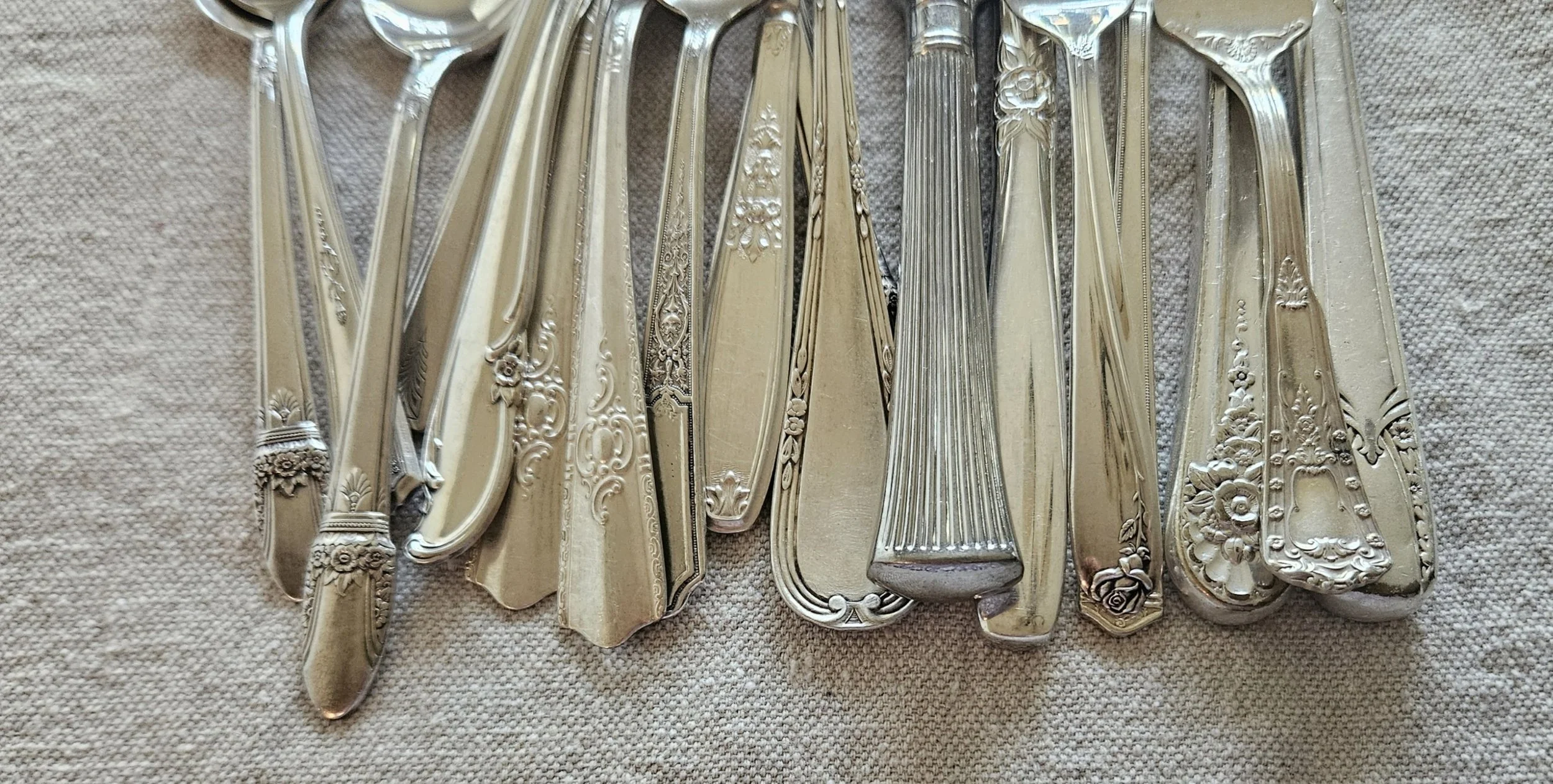 A collection of vintage silverware including knives, forks, spoons, and serving utensils, arranged on a textured surface.